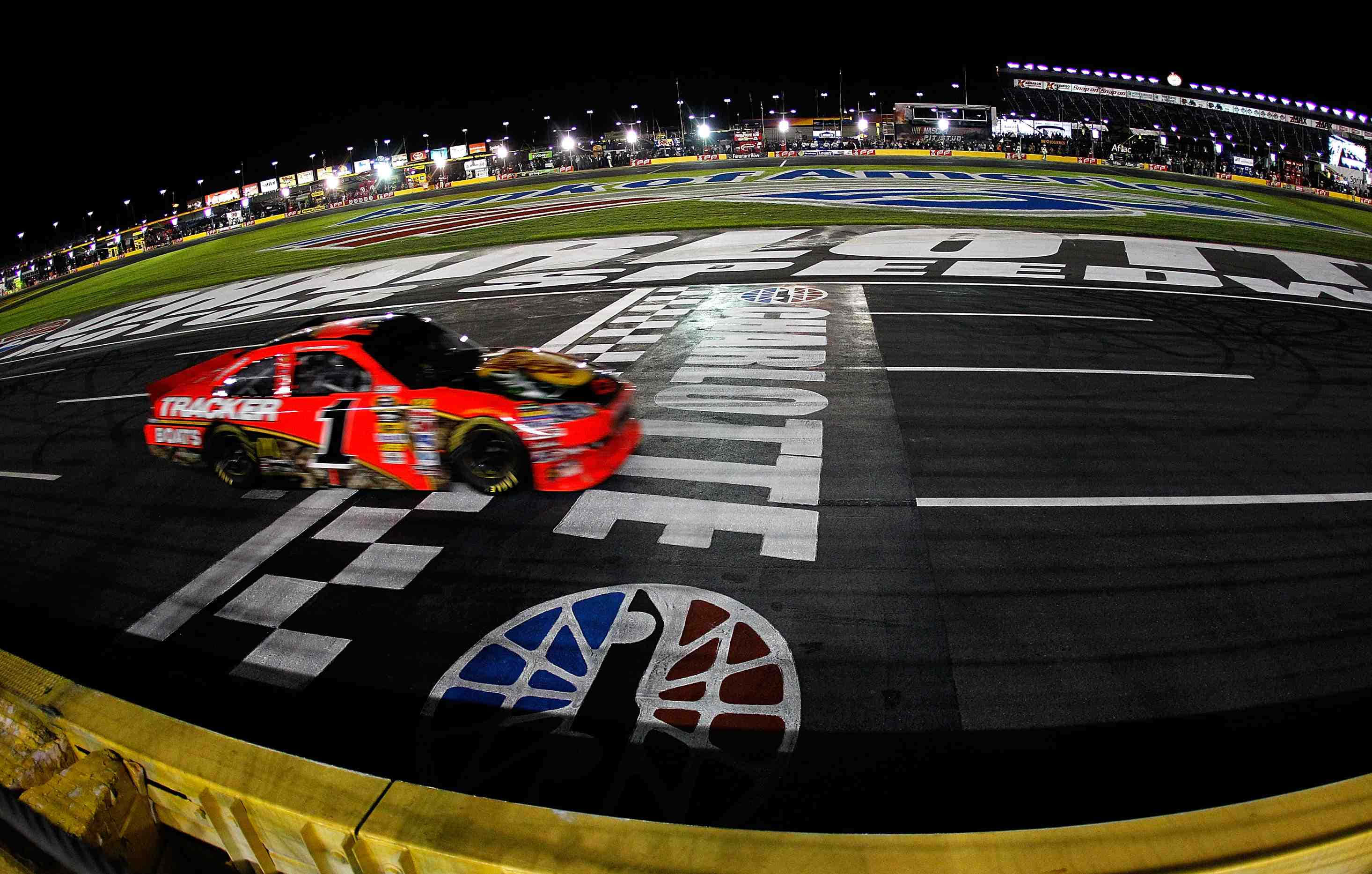 nascar 桌布 壁紙 — 一輛紅色賽車在夜間賽道上，於明亮的體育場燈光下越過方格終點線。