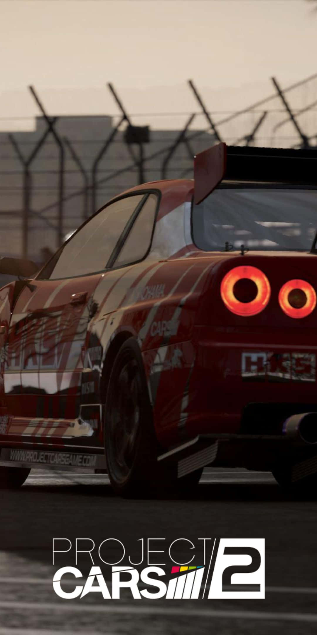 Pixel 3 Project Cars 2 桌布 壁紙 — 一輛紅色賽車在朦朧的天空下，沿著由鐵絲網圍欄環繞的賽道疾馳，尾燈閃閃發光。