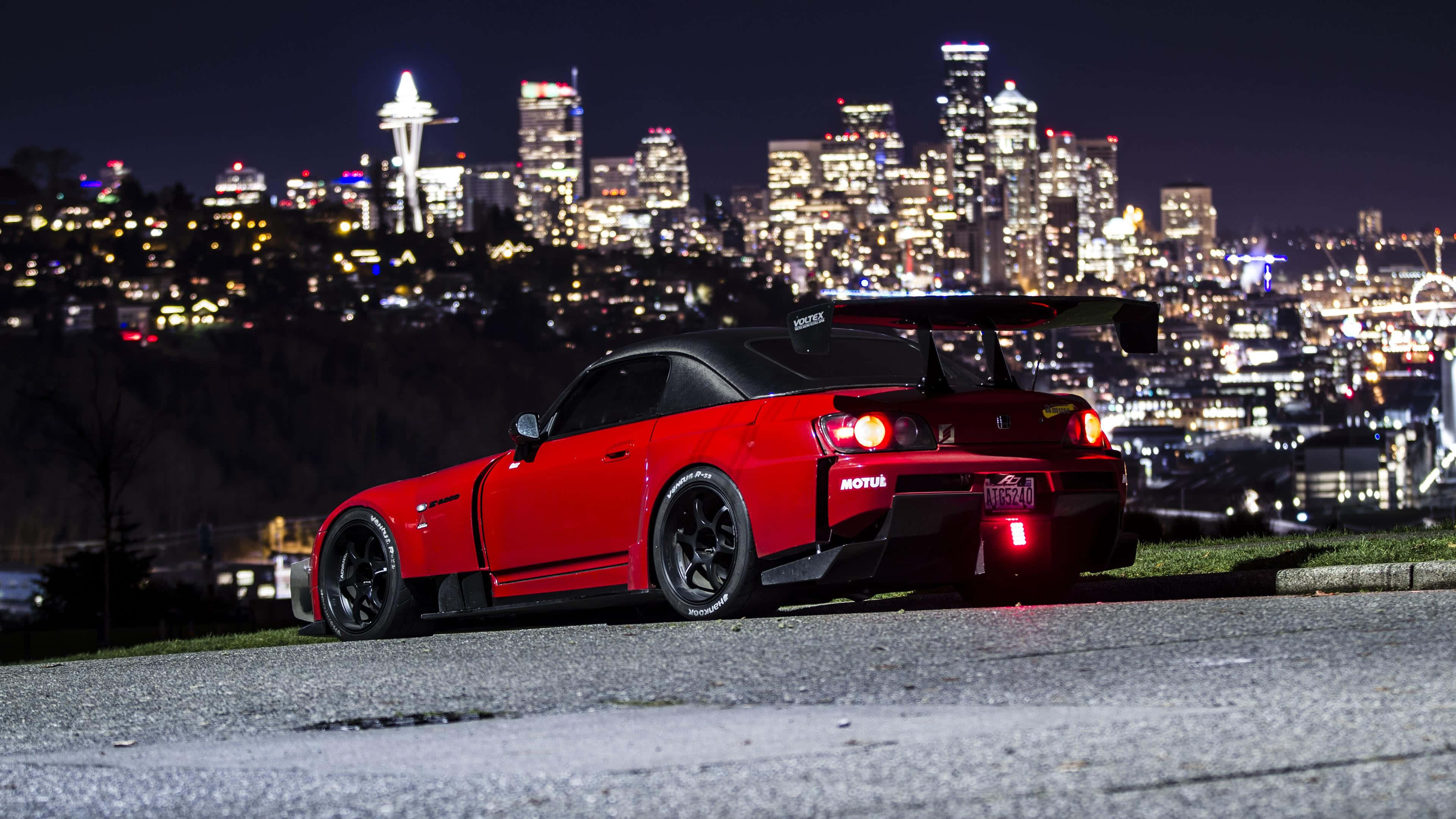 Honda S2000 桌布 壁紙 — 一輛紅色跑車，帶有發光的尾燈，停在山丘上，俯瞰西雅圖夜間燈火通明的天際線。