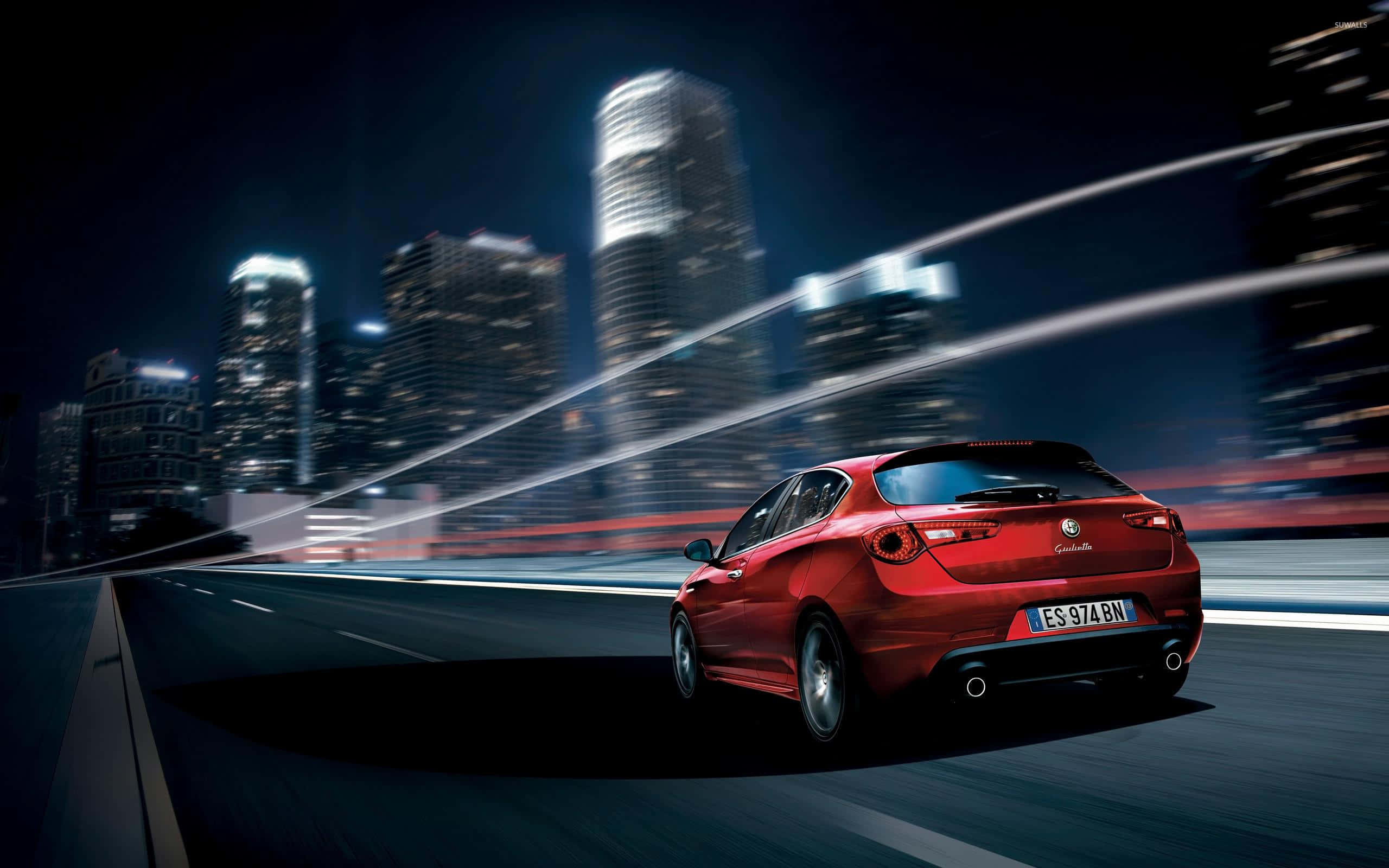 Alfa Romeo Giulietta 桌布 壁紙 — 一輛紅色跑車在夜晚穿過霓虹燈閃爍的城市，模糊的摩天大樓和光跡。