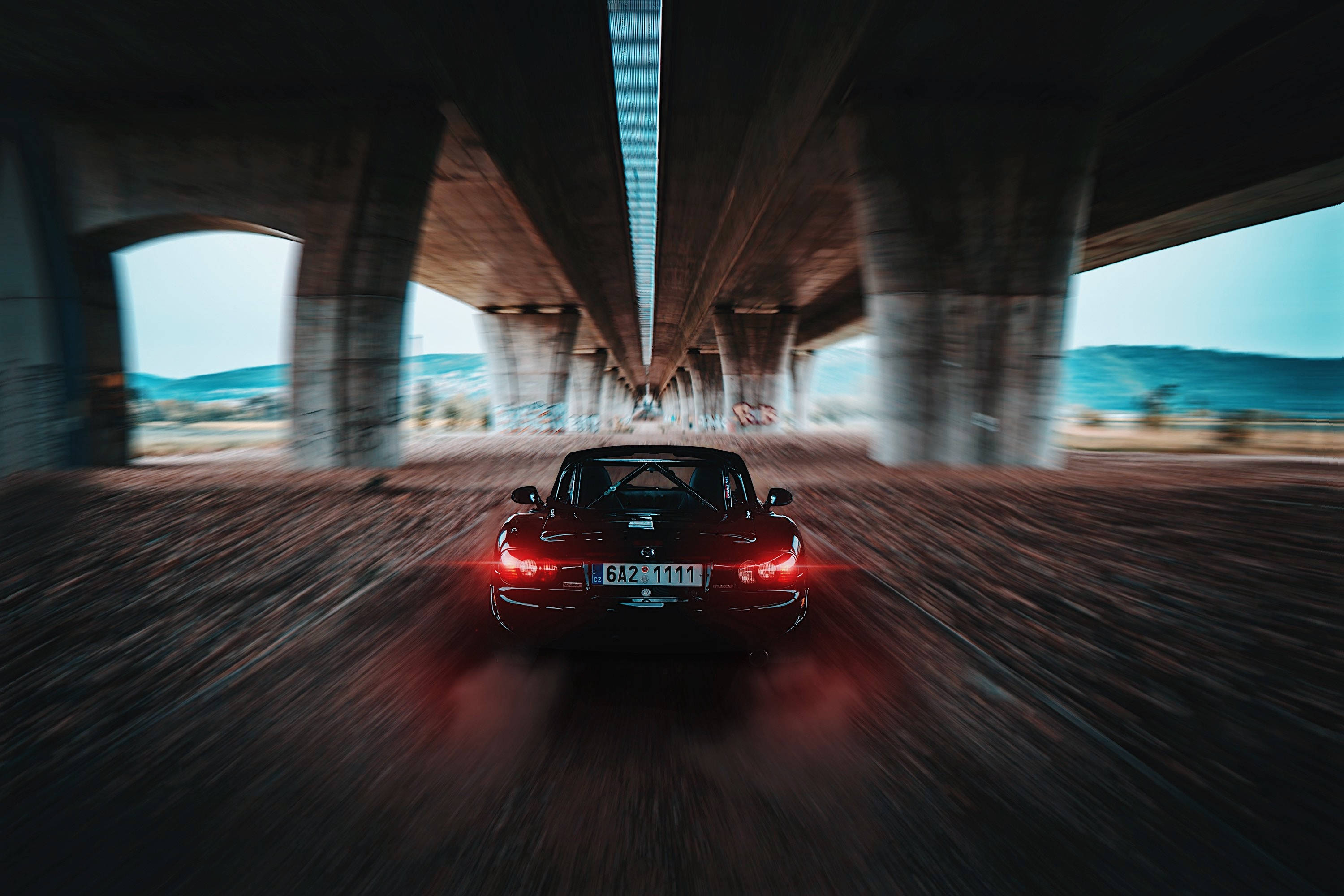 Mazda 桌布 壁紙 — 一輛紅色跑車在混凝土天橋下高速行駛，帶有模糊的動態和發光的尾燈。