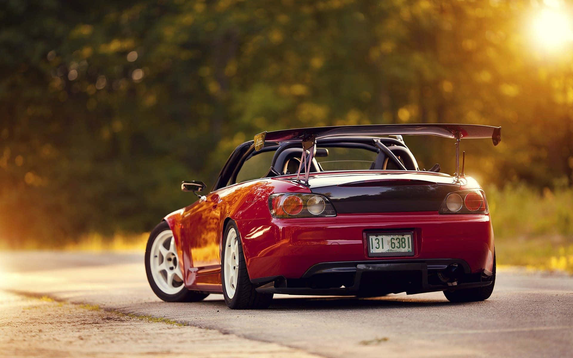Honda S2000 桌布 壁紙 — 一輛紅色跑車帶有大型尾翼，在黃金時刻停泊在道路上，背景有樹木。