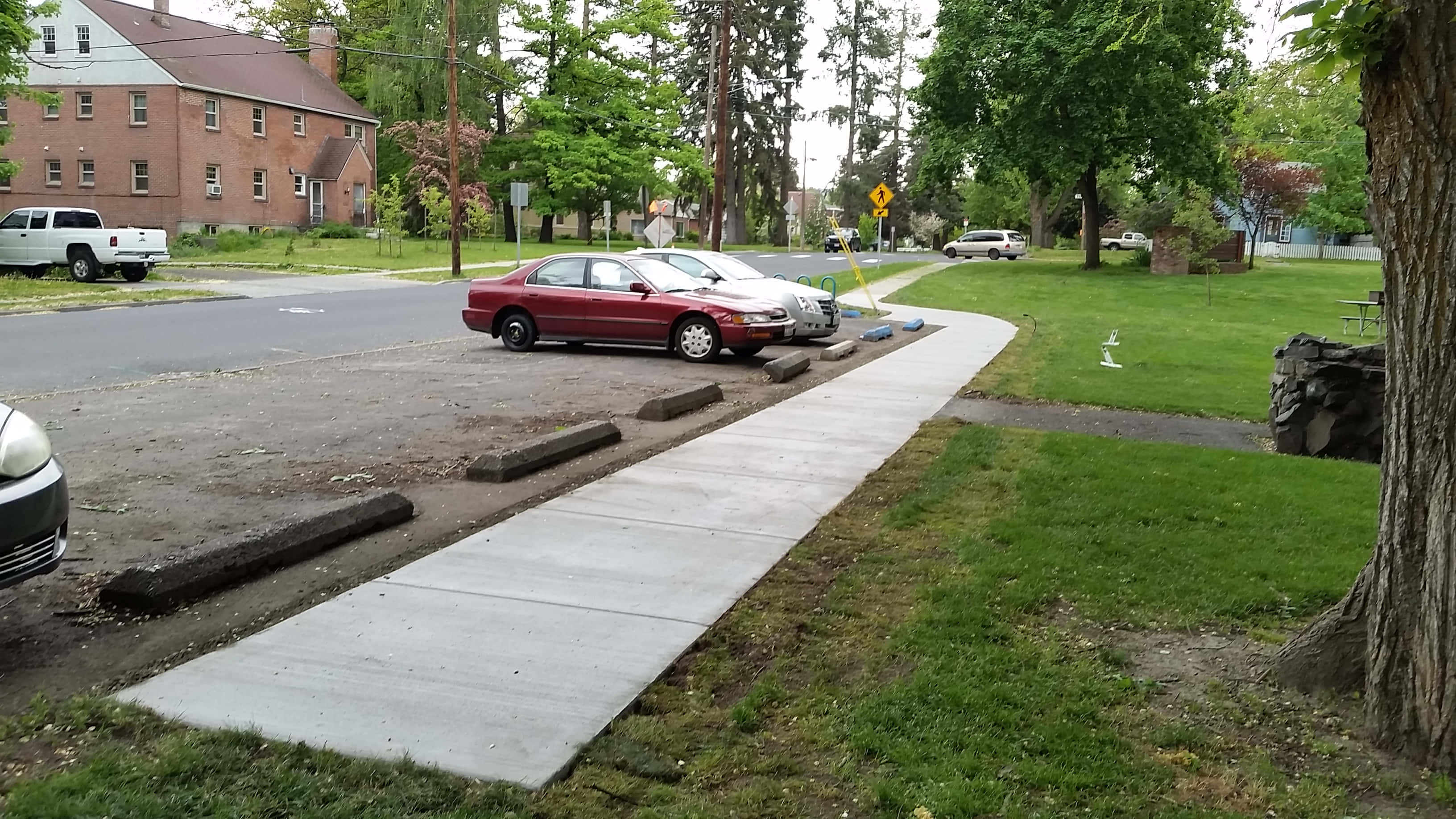 Sidewalk 桌布 壁紙 — 一輛紅色轎車停泊在寧靜郊區住宅區的碎石地上，旁邊是混凝土人行道，周圍有草地和樹木。