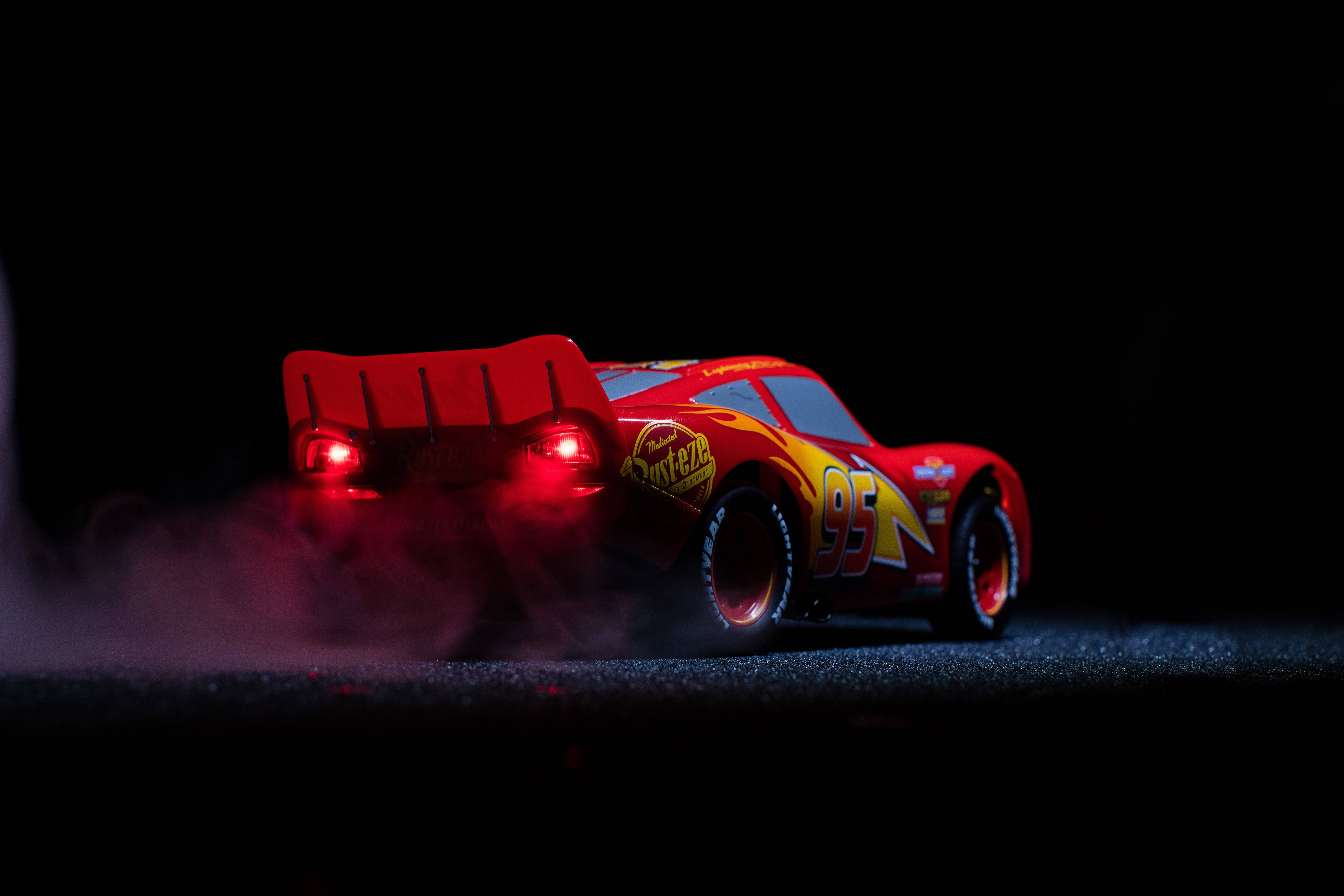 Pixar 桌布 壁紙 — 一輛紅色閃電麥坤玩具車，在深色瀝青路面上，車尾燈發光並有煙霧從車尾飄出。