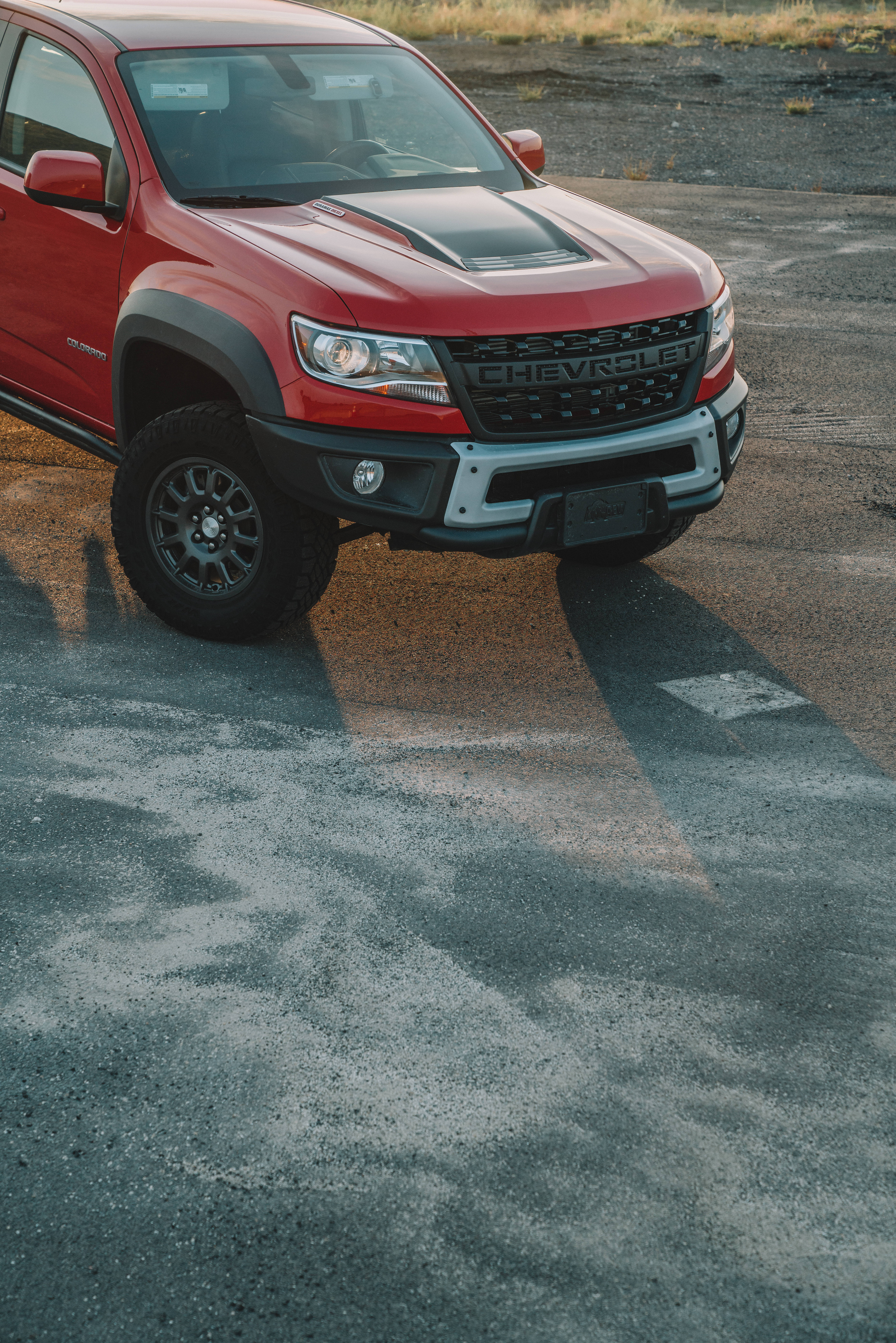 Chevrolet 桌布 壁紙 — 一輛紅色雪佛蘭Colorado ZR2皮卡車停在裂開的瀝青路上，溫暖的黃金時段光線投下長長的陰影。