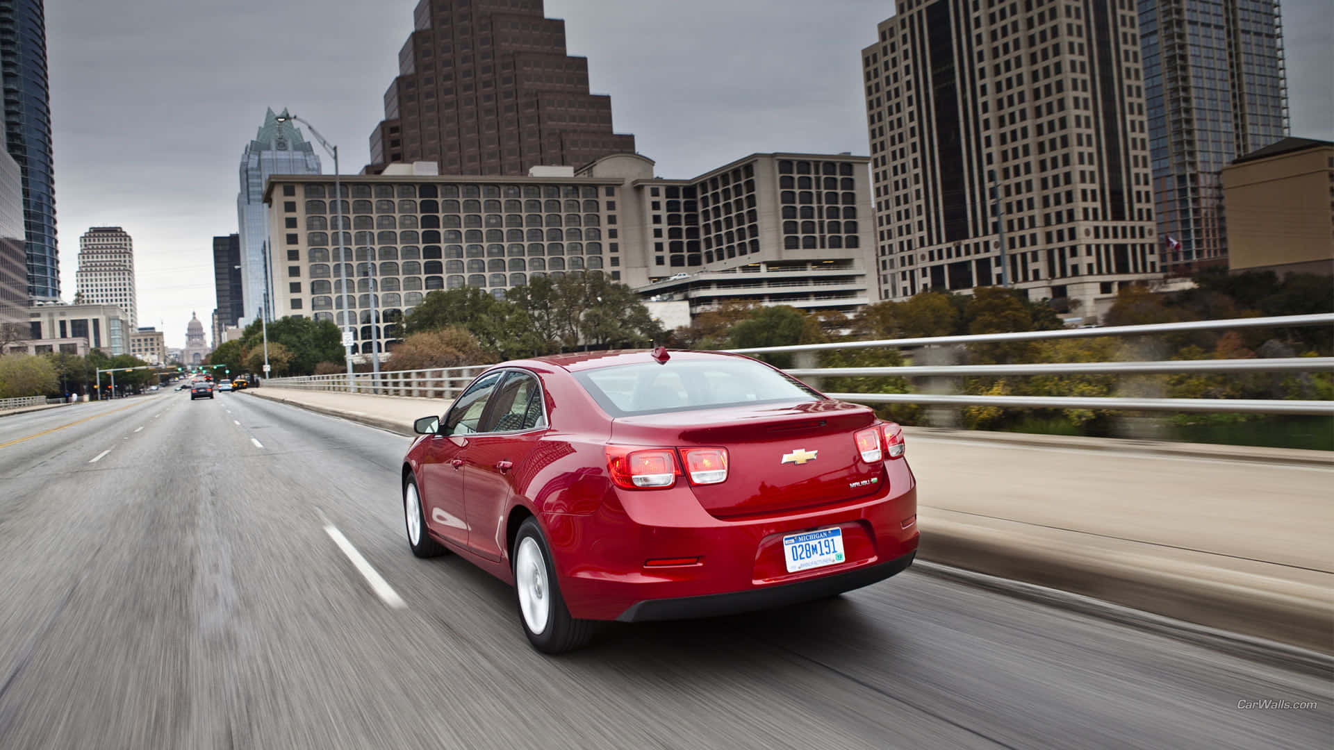 Chevy Malibu 桌布 壁紙 — 一輛紅色雪佛蘭Malibu在陰天籠罩下，行駛於摩天大樓林立的城市橋樑上。