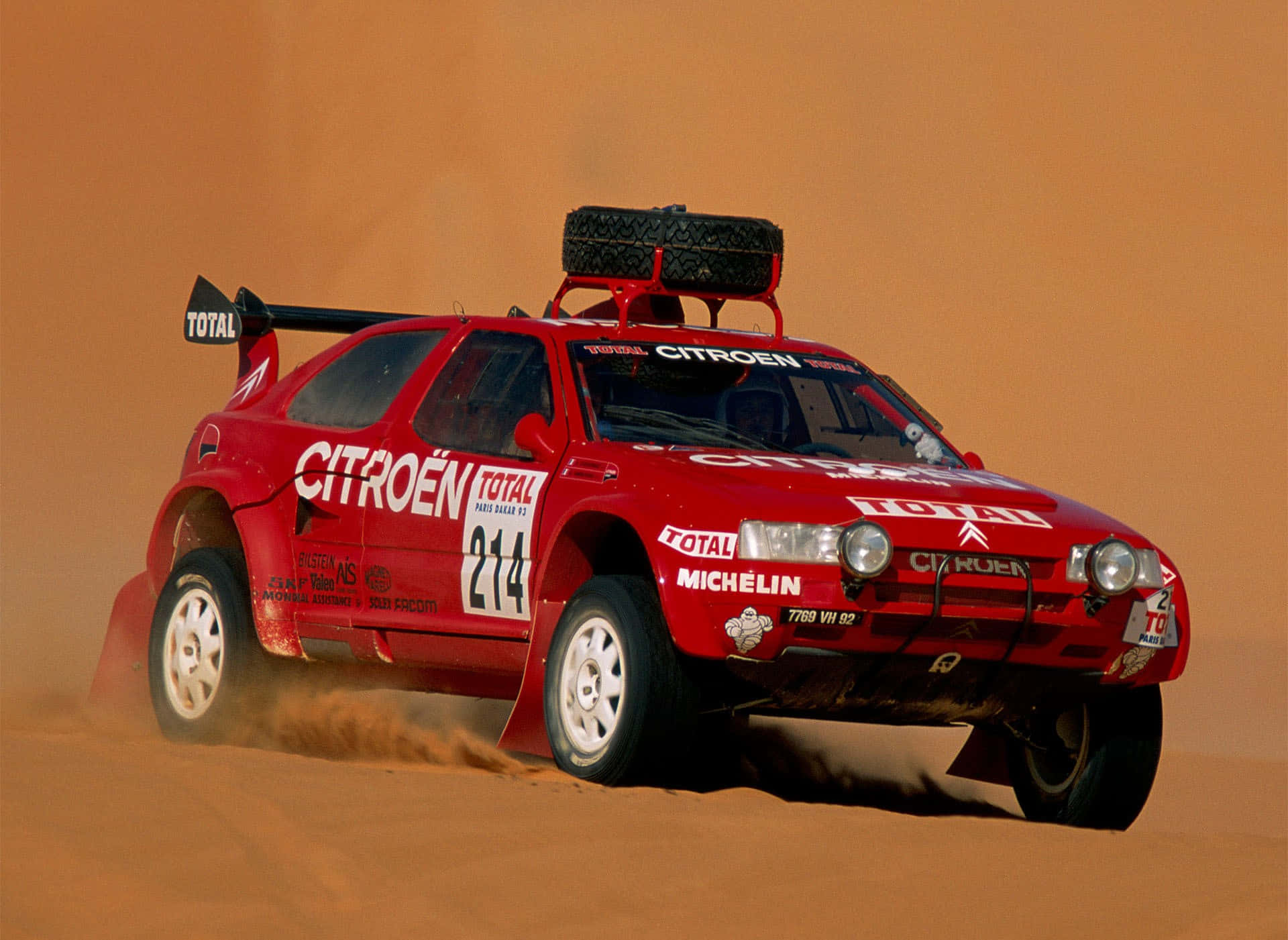 Citroen Zx 桌布 壁紙 — 一輛紅色雪鐵龍拉力賽車在明亮的日光下，高速駛過廣闊的沙漠沙丘，揚起沙塵。