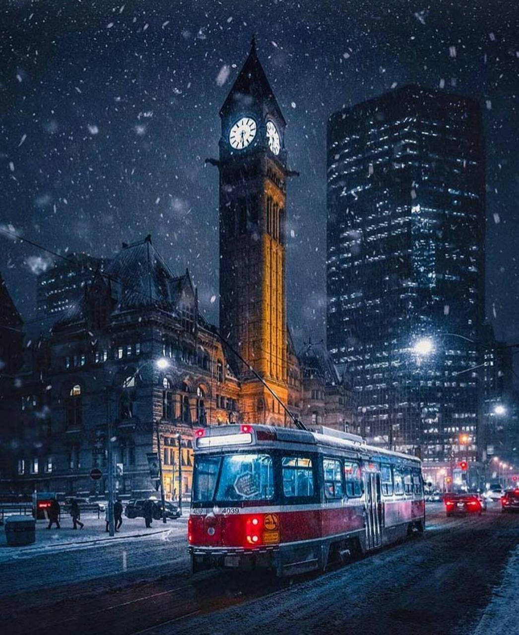 Ontario 桌布 壁紙 — 一輛紅色電車在雪夜中滑行，城市中歷史悠久的鐘樓和現代摩天大樓在飄落的雪花下閃閃發光。
