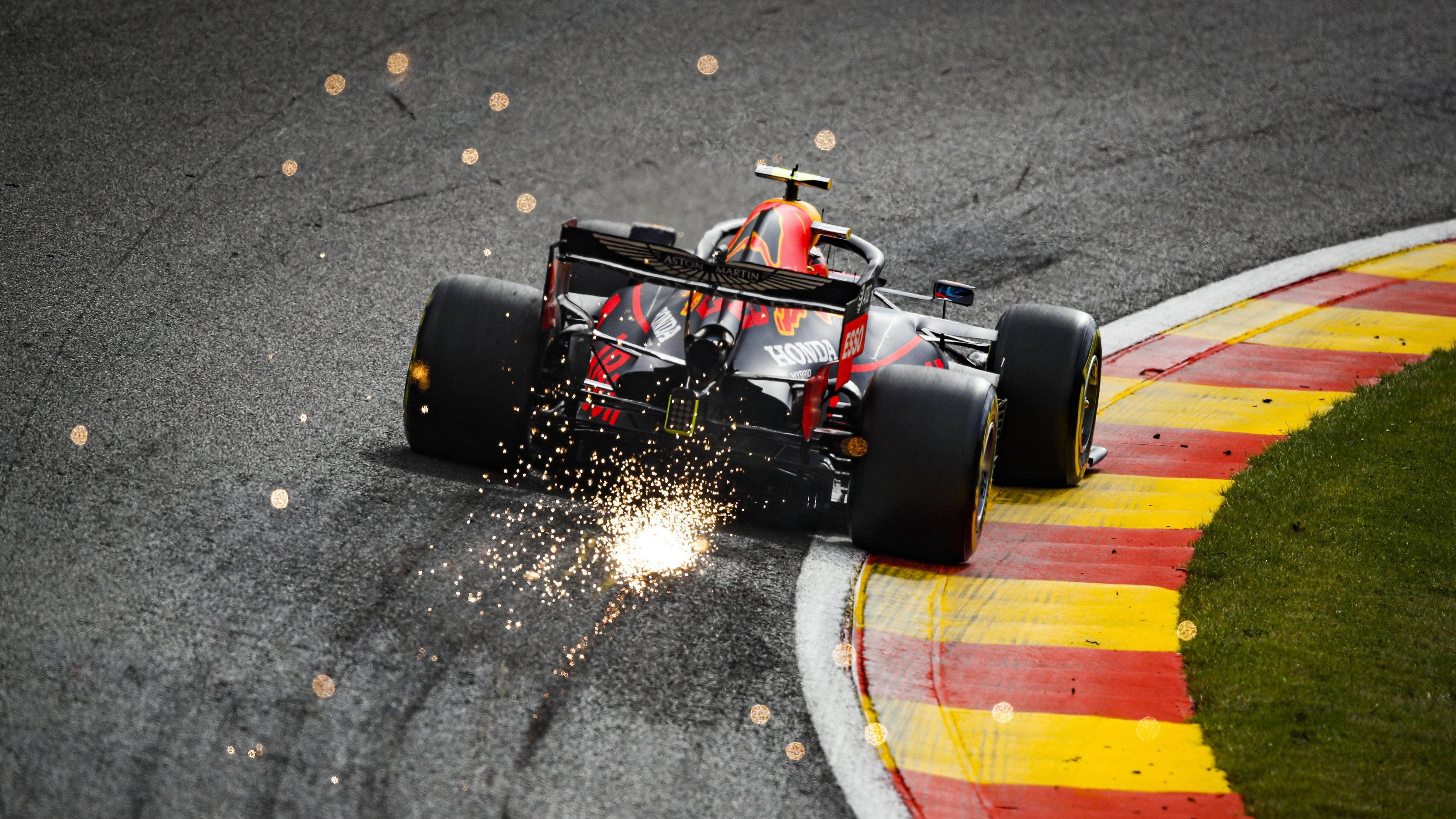 Auto Racing 桌布 壁紙 — 一輛紅黑相間的F1賽車在濕滑彎道上劃過，邊緣有紅、黃、綠色，戲劇性地迸發火花。