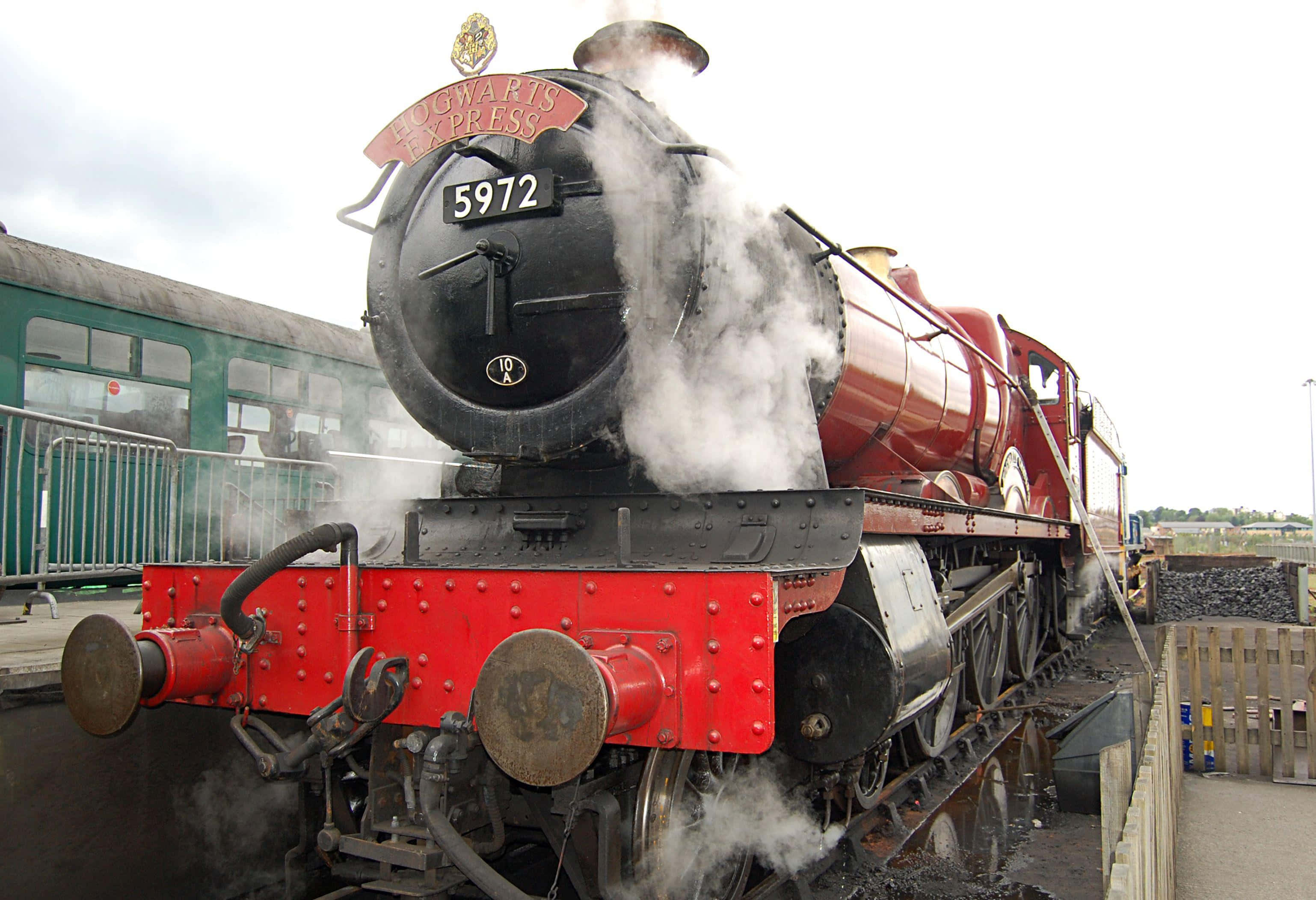 The Hogwarts Express Train 桌布 壁紙 — 一輛紅黑相間的霍格華茲特快蒸汽火車在陰天下的月台停靠，噴出白色蒸氣。