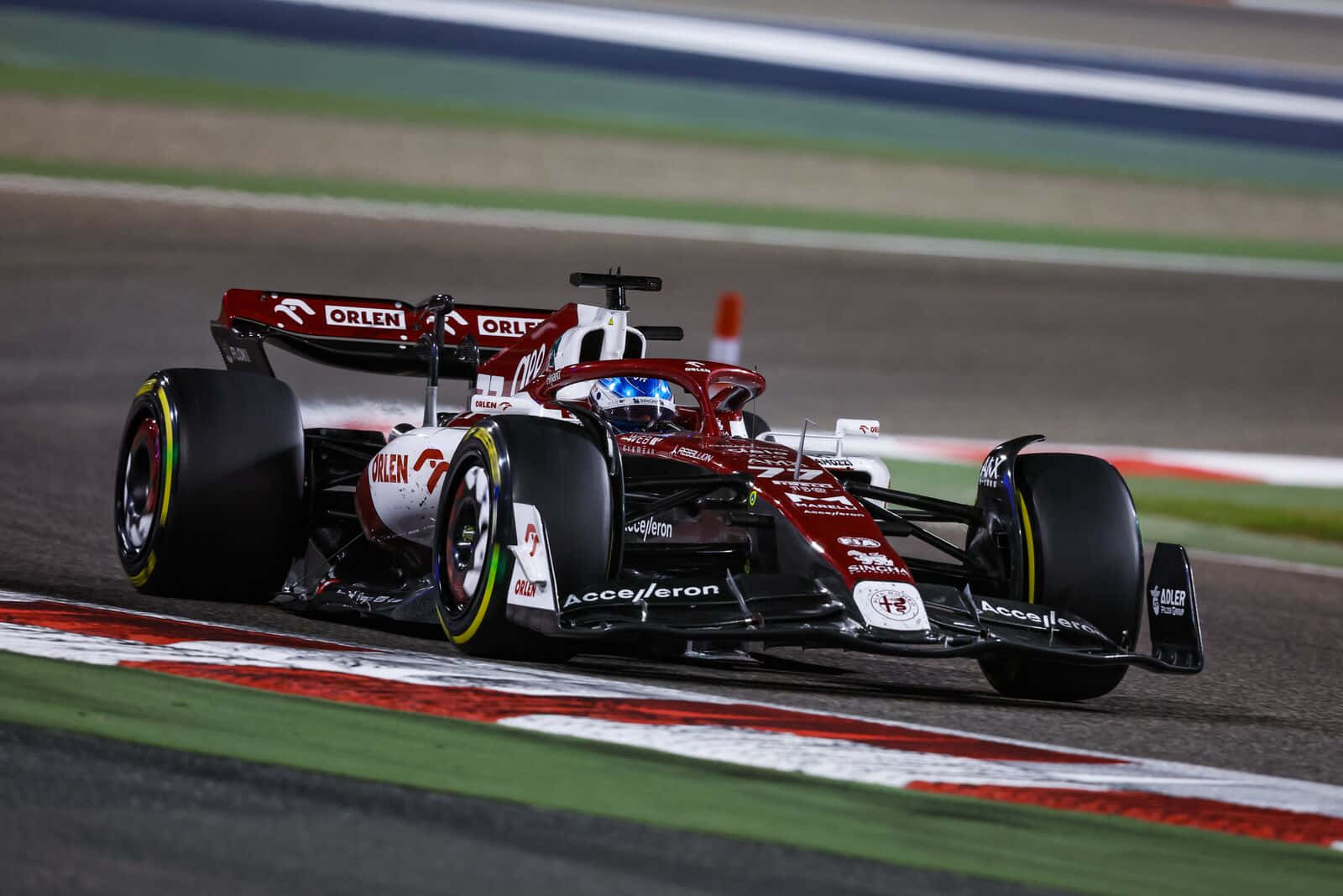 F1 2016 桌布 壁紙 — 一輛紅黑配色的F1賽車在夜間賽道上疾馳，車頭燈閃爍，贊助商標誌清晰可見。
