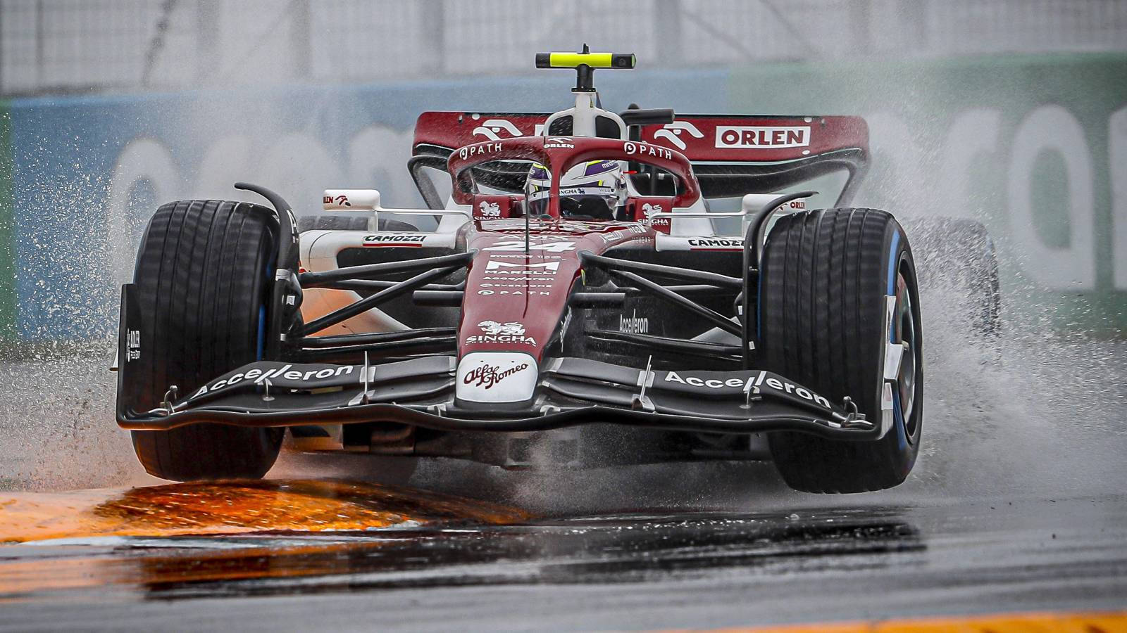 F1 桌布 壁紙 — 一輛紅黑配色的F1賽車在濕滑的彎道上飛馳，濺起水花和橙色賽道標記。