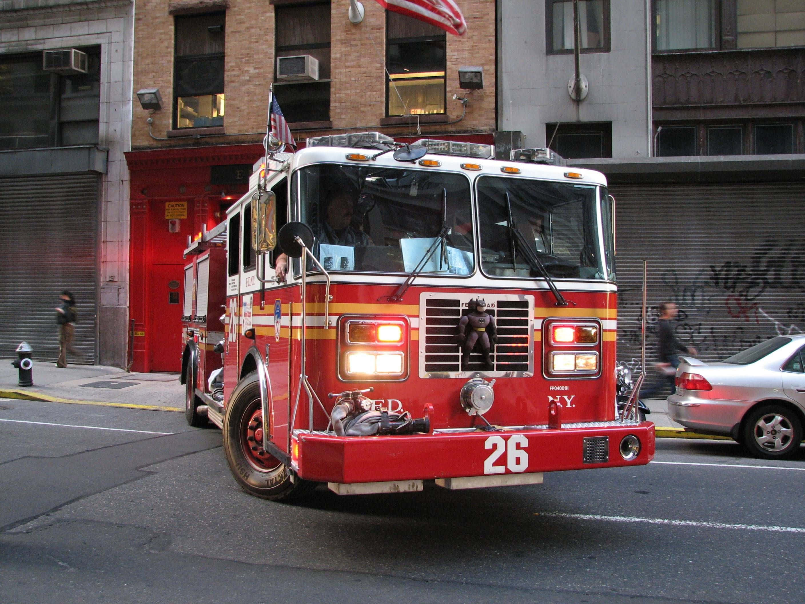Fire Truck 桌布 壁紙 — 一輛紐約市紅色消防車（編號26）停在城市街道上，靠近一座有磚砌建築和行人的消防局。