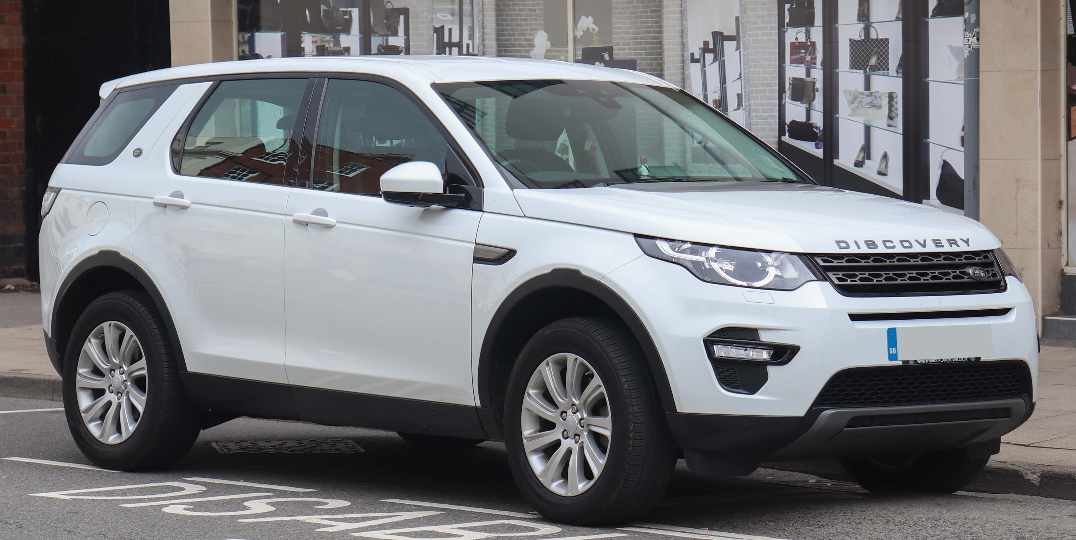 Land Rover Discovery 桌布 壁紙 — 一輛純白色 Land Rover Discovery SUV 停放在城市街道上，背景有商店門面。