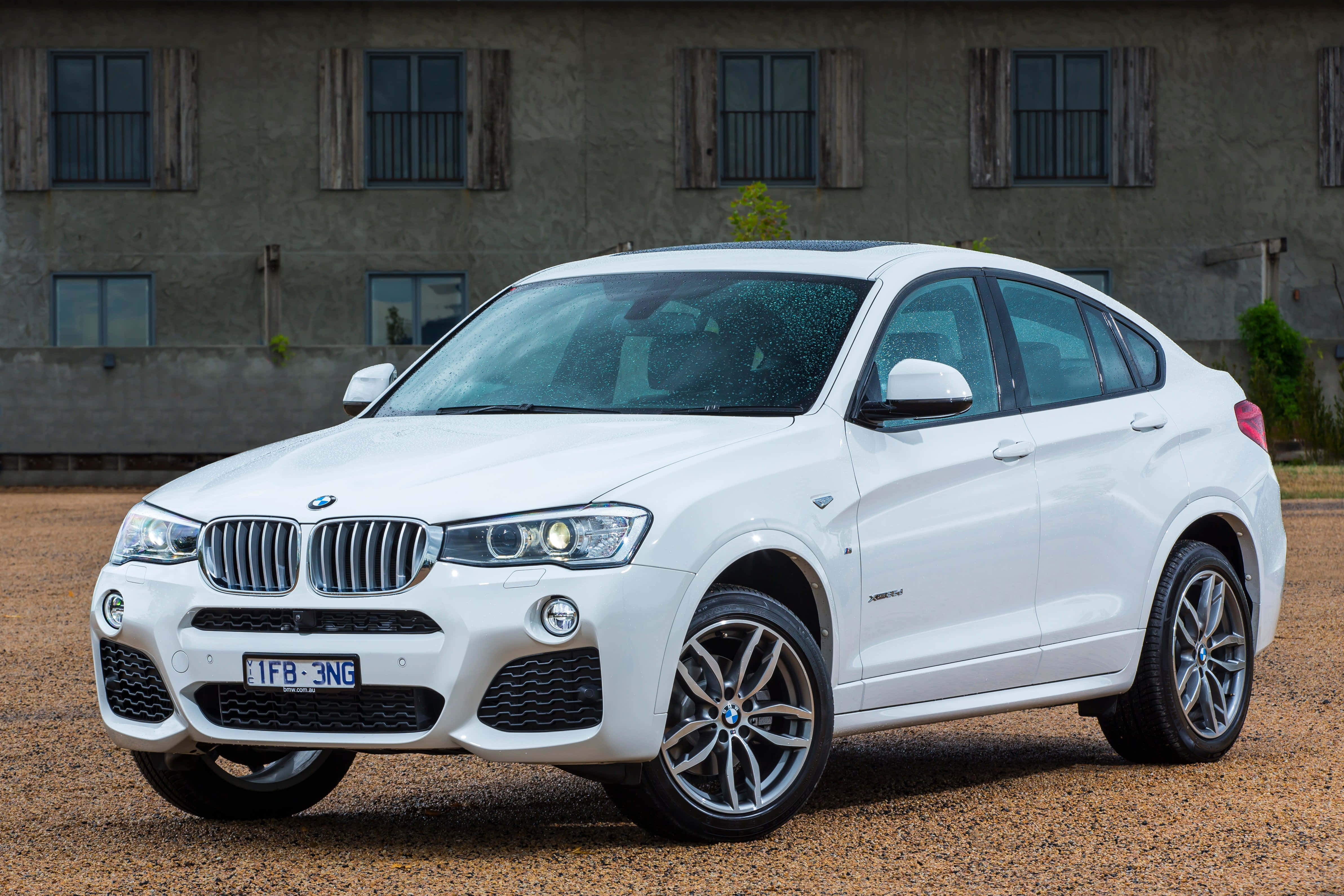 Bmw X4 桌布 壁紙 — 一輛純白色BMW X4 SUV停泊在碎石路上，前方是一座有木製百葉窗的風化建築物。