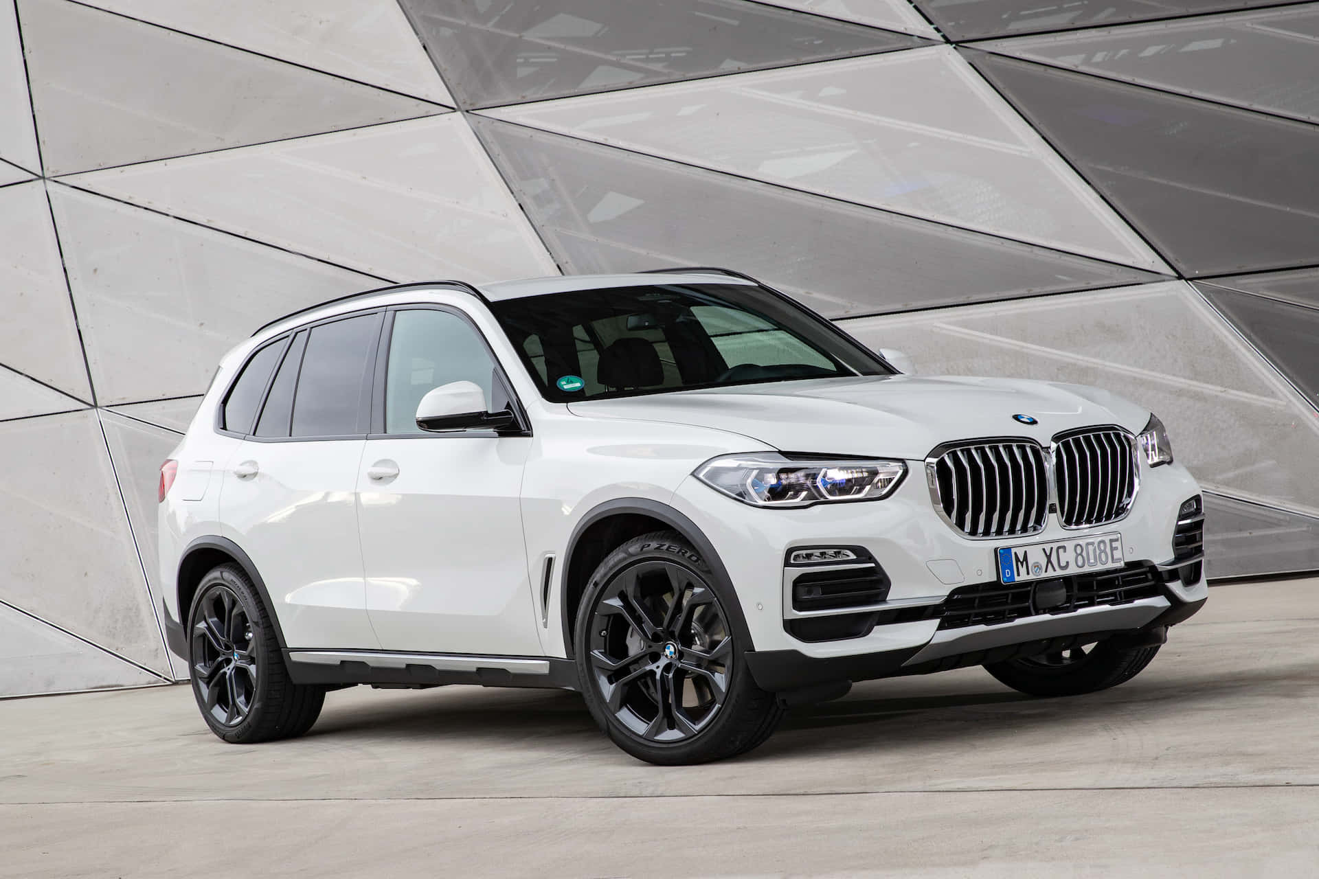 Bmw X5 桌布 壁紙 — 一輛純白色BMW X5 SUV搭配黑色輪圈，自信地矗立在現代幾何玻璃與混凝土建築外牆前。