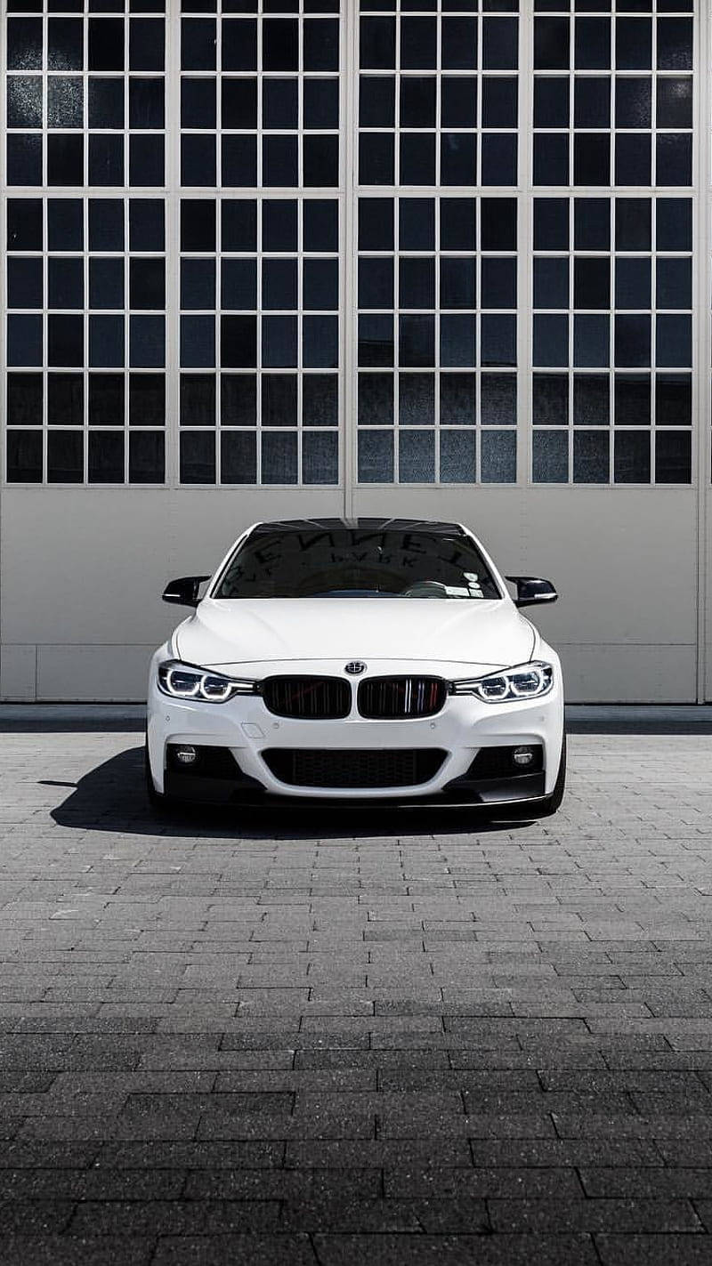 m 桌布 壁紙 — 一輛純白色BMW跑車停放在灰色磚鋪路面上，前面是一棟有大型格窗的工業建築。