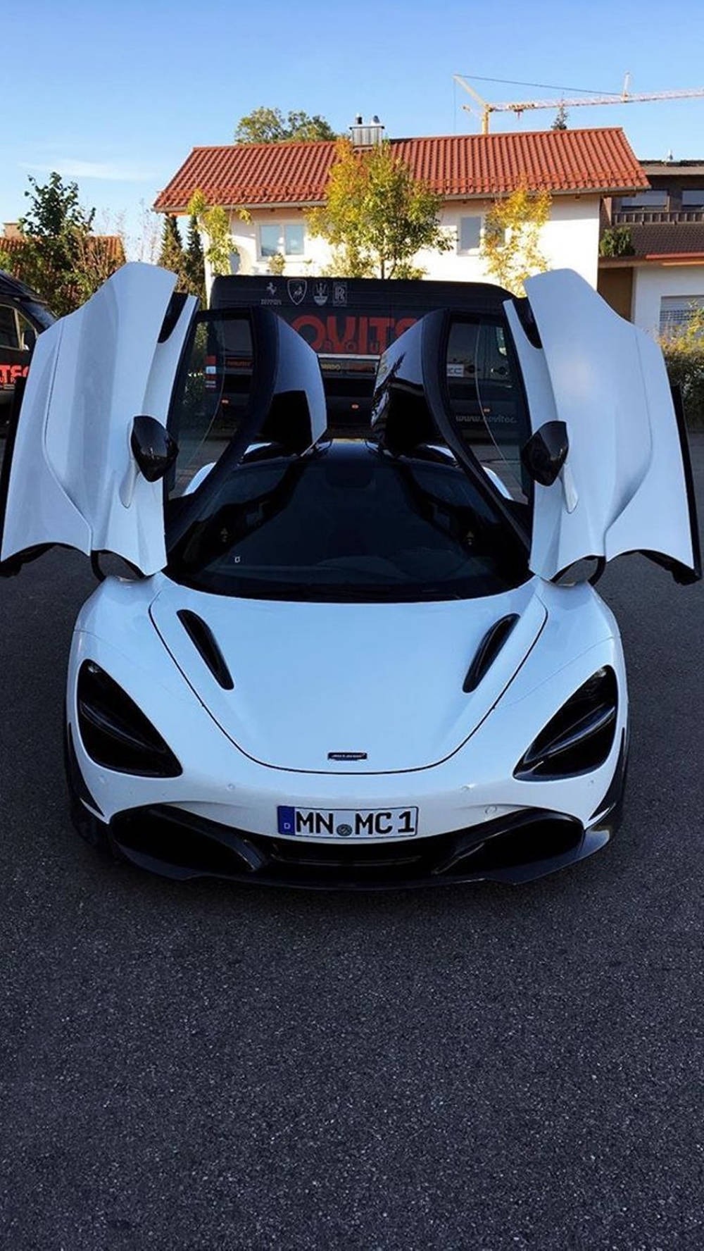 跑車 桌布 壁紙 — 一輛純白色McLaren跑車，鷗翼車門打開，停放在住宅大樓前的柏油路上，天空晴朗湛藍。
