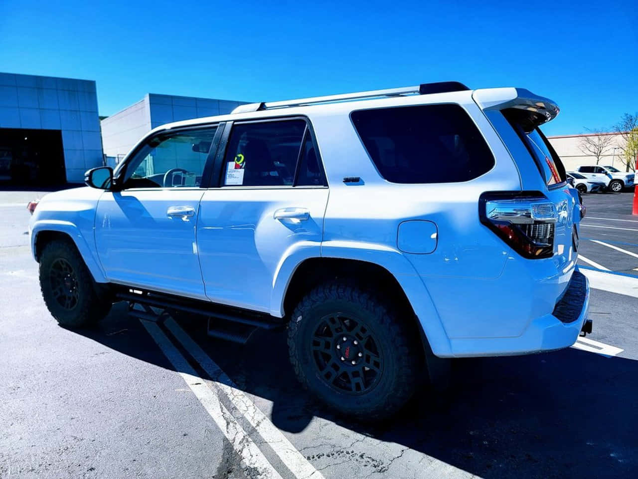 2023 Toyota 4runner 桌布 壁紙 — 一輛純白色SUV配黑色輪圈，停在晴朗藍天下的陽光停車場。
