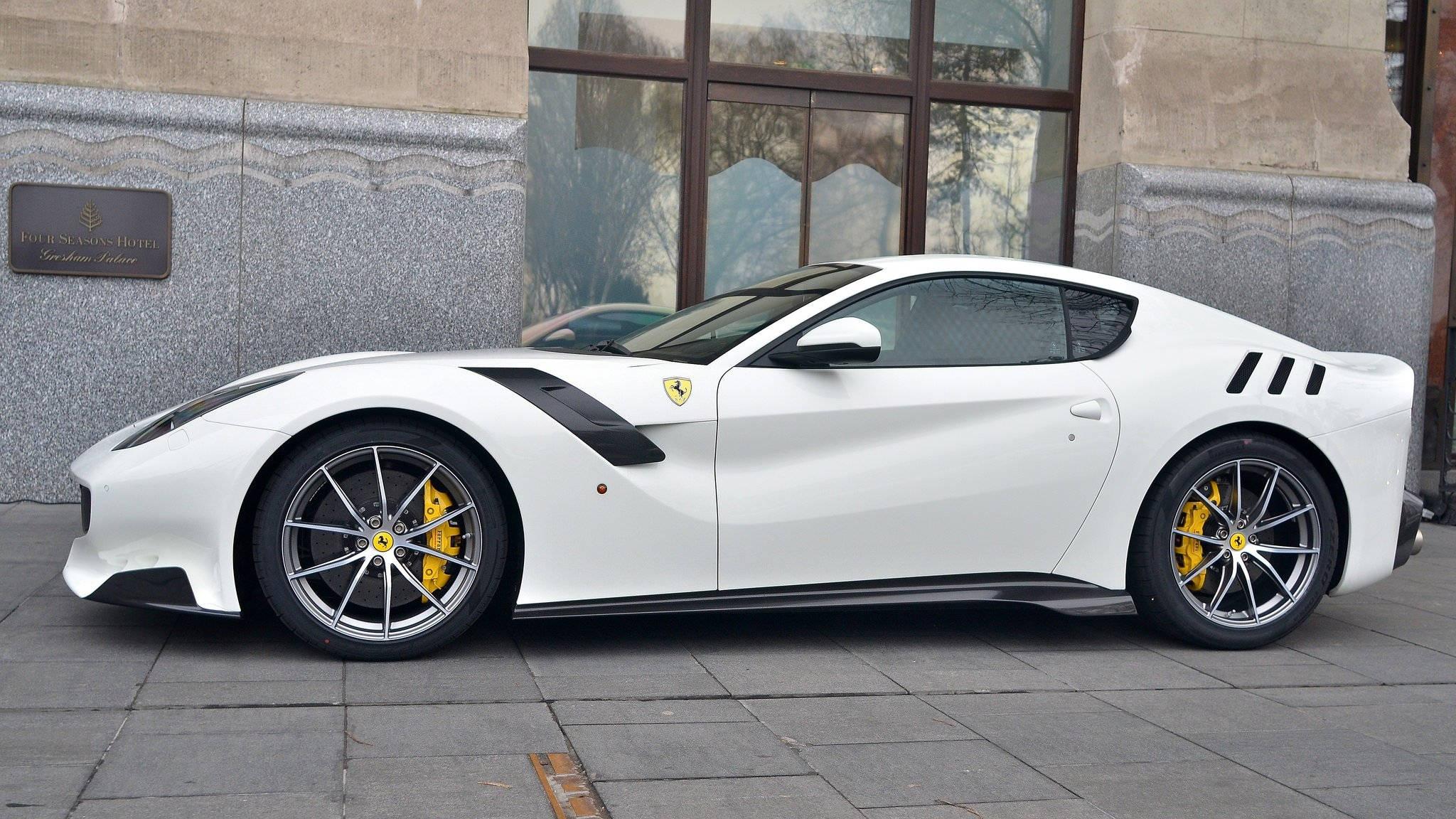 white ferrari 桌布 壁紙 — 一輛純白色法拉利跑車配黃色制動卡鉗，停泊在現代建築旁邊的石板路上。