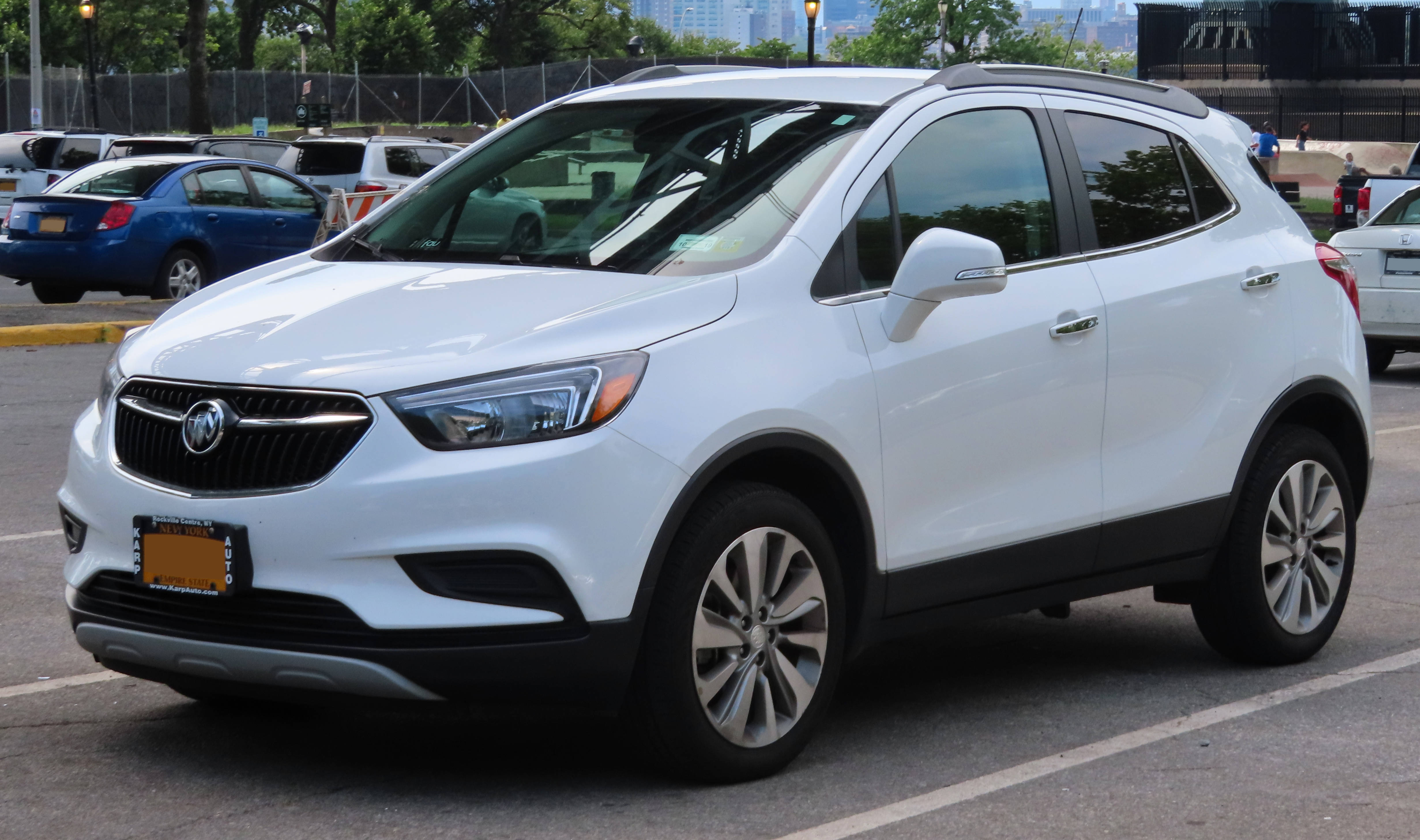Buick 桌布 壁紙 — 一輛純白色的 Buick Encore SUV 停放在陽光明媚的城市空地，背景有其他汽車和城市建築。