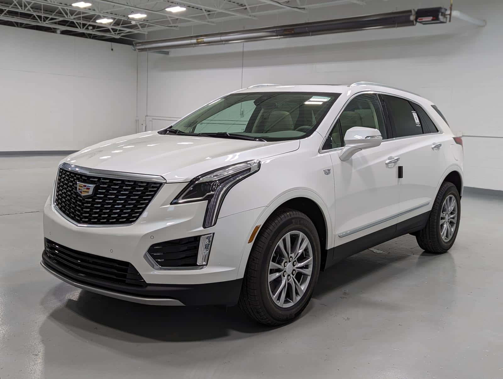 Cadillac Xt5 桌布 壁紙 — 一輛純白色的 Cadillac XT5 SUV 在明亮、簡約的室內展示廳中展示，地板為拋光混凝土地面，天花桁架外露。
