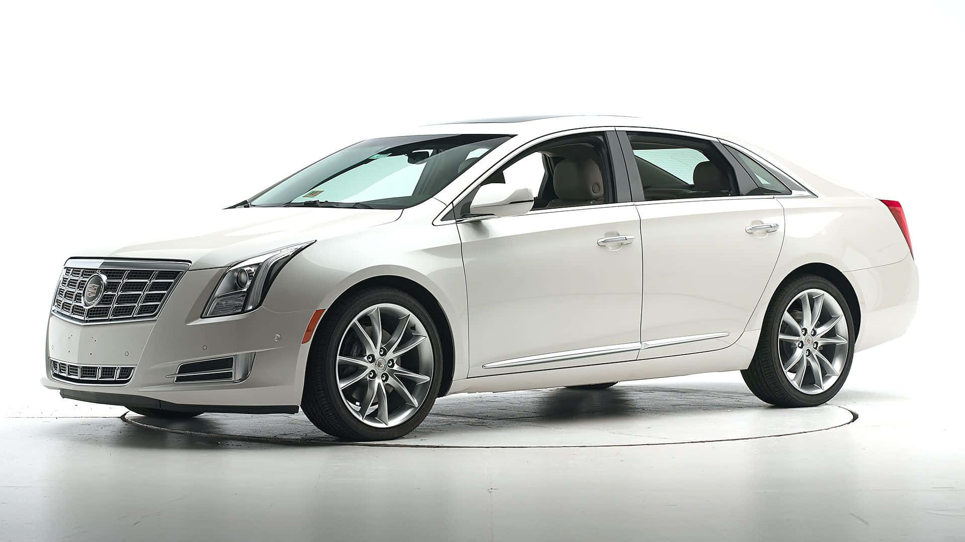 Cadillac Xts 桌布 壁紙 — 一輛純白色的 Cadillac XTS 轎車在明亮的攝影棚燈光下閃耀，展現其流線型的現代設計和拋光合金輪圈。