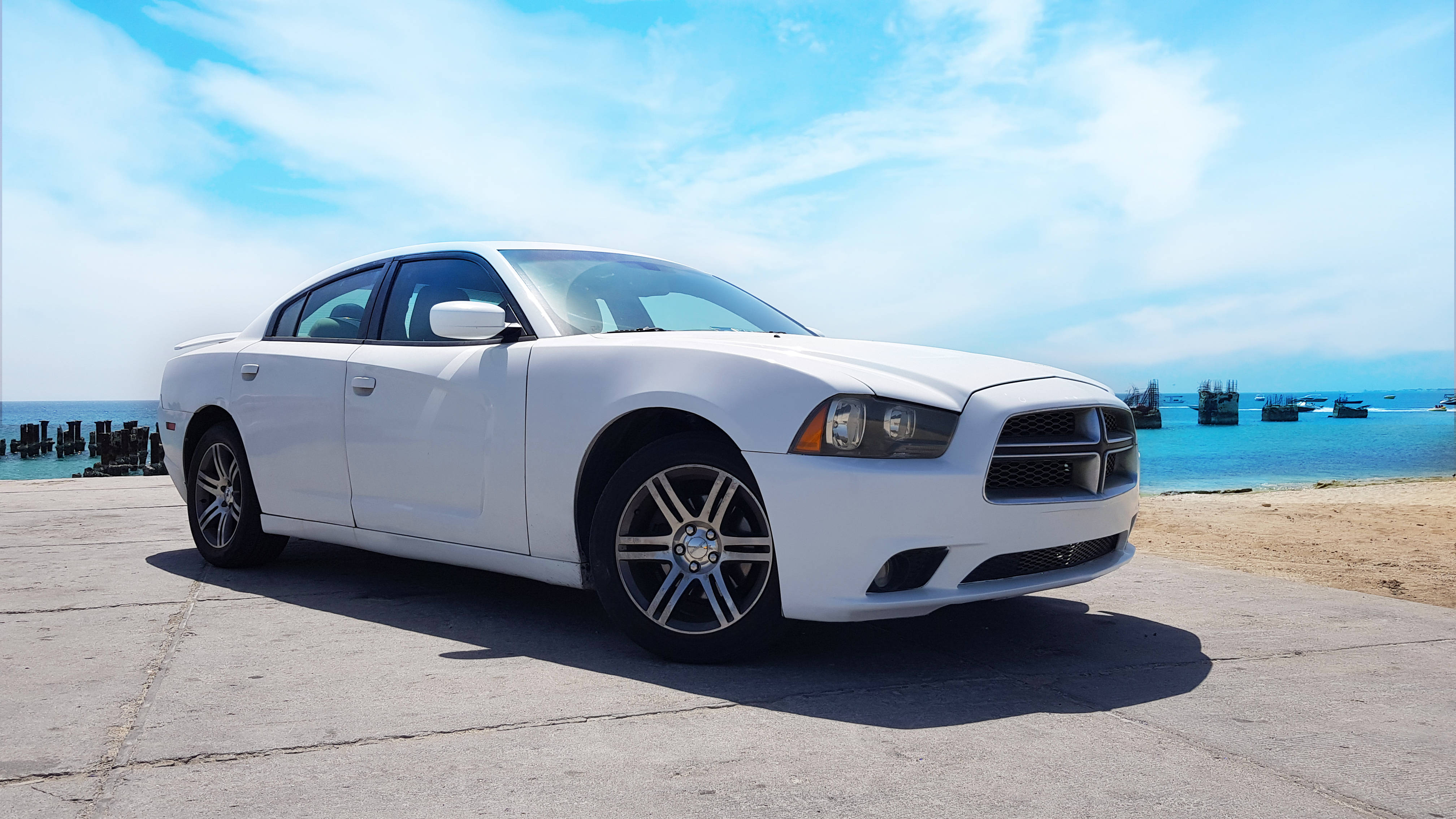 Challenger 桌布 壁紙 — 一輛純白色的 Dodge Charger 停泊在混凝土碼頭上，碧綠色的海洋和遠處的船隻在明亮的藍天下。