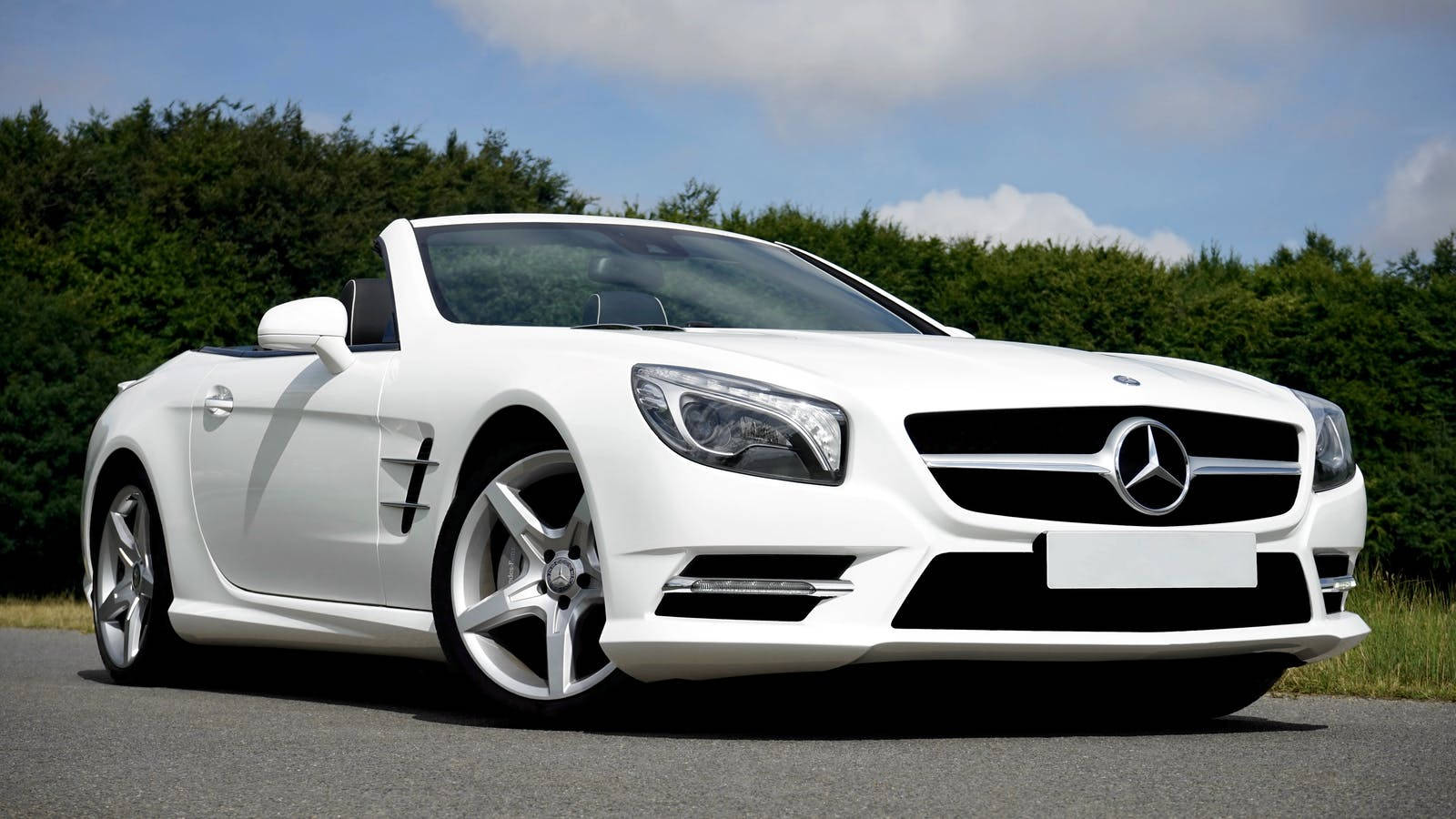 跑車 桌布 壁紙 — 一輛純白色的 Mercedes-Benz SL 敞篷車停在柏油路上，背景是茂密的綠樹和藍天。