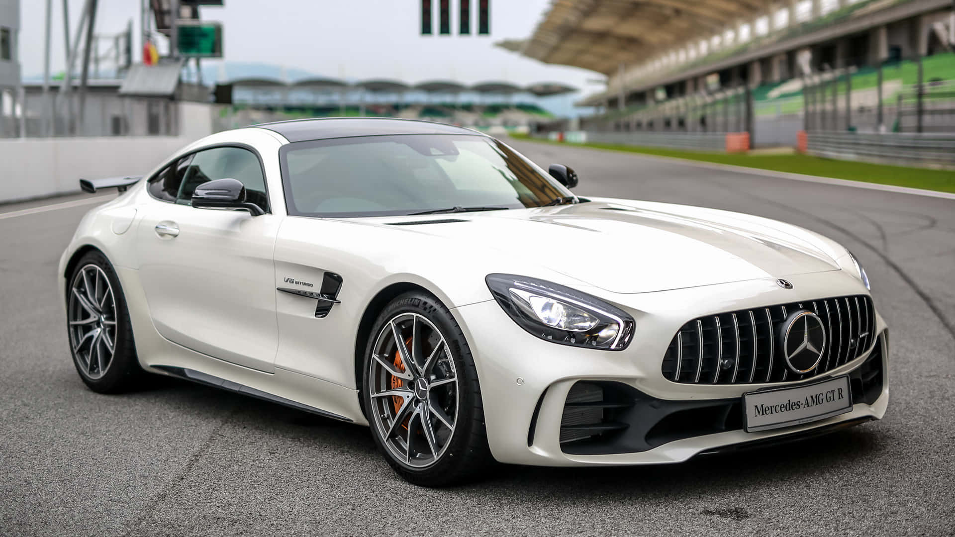 汽車 桌布 壁紙 — 一輛純白色的 Mercedes-AMG GT R 跑車在賽道上閃閃發光，背景有看台和綠色圍欄。