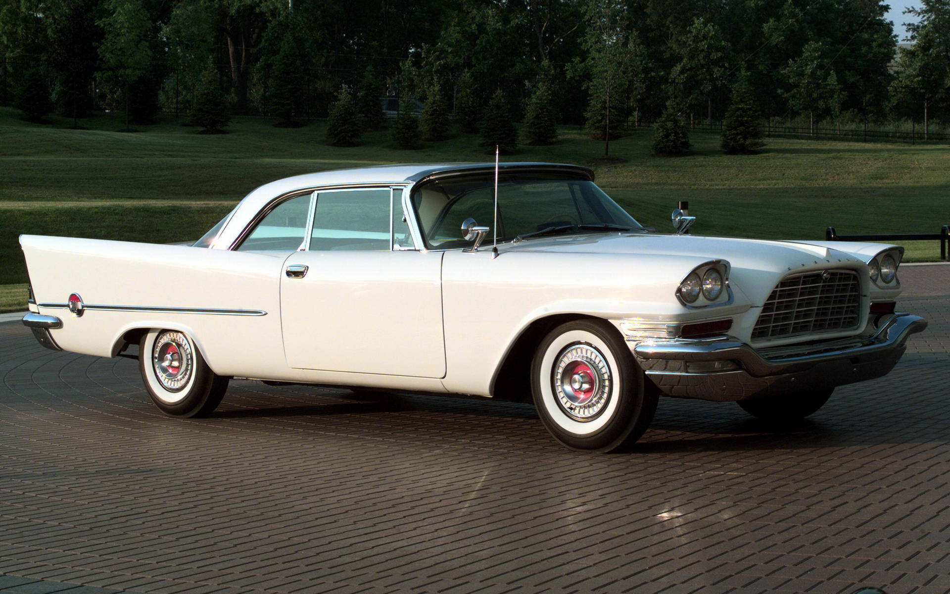 Chrysler 桌布 壁紙 — 一輛純白色的1950年代經典汽車在柔和陽光下，於鋪砌的車道上閃閃發光，周圍環繞著茂密的綠樹。