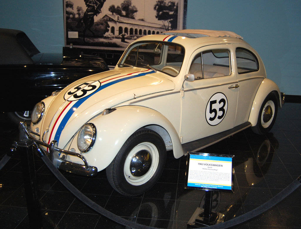 Herbie 桌布 壁紙 — 一輛純白色的1963年福斯金龜車賽車，帶有藍紅條紋和53號碼，在博物館的反射地板上展出。