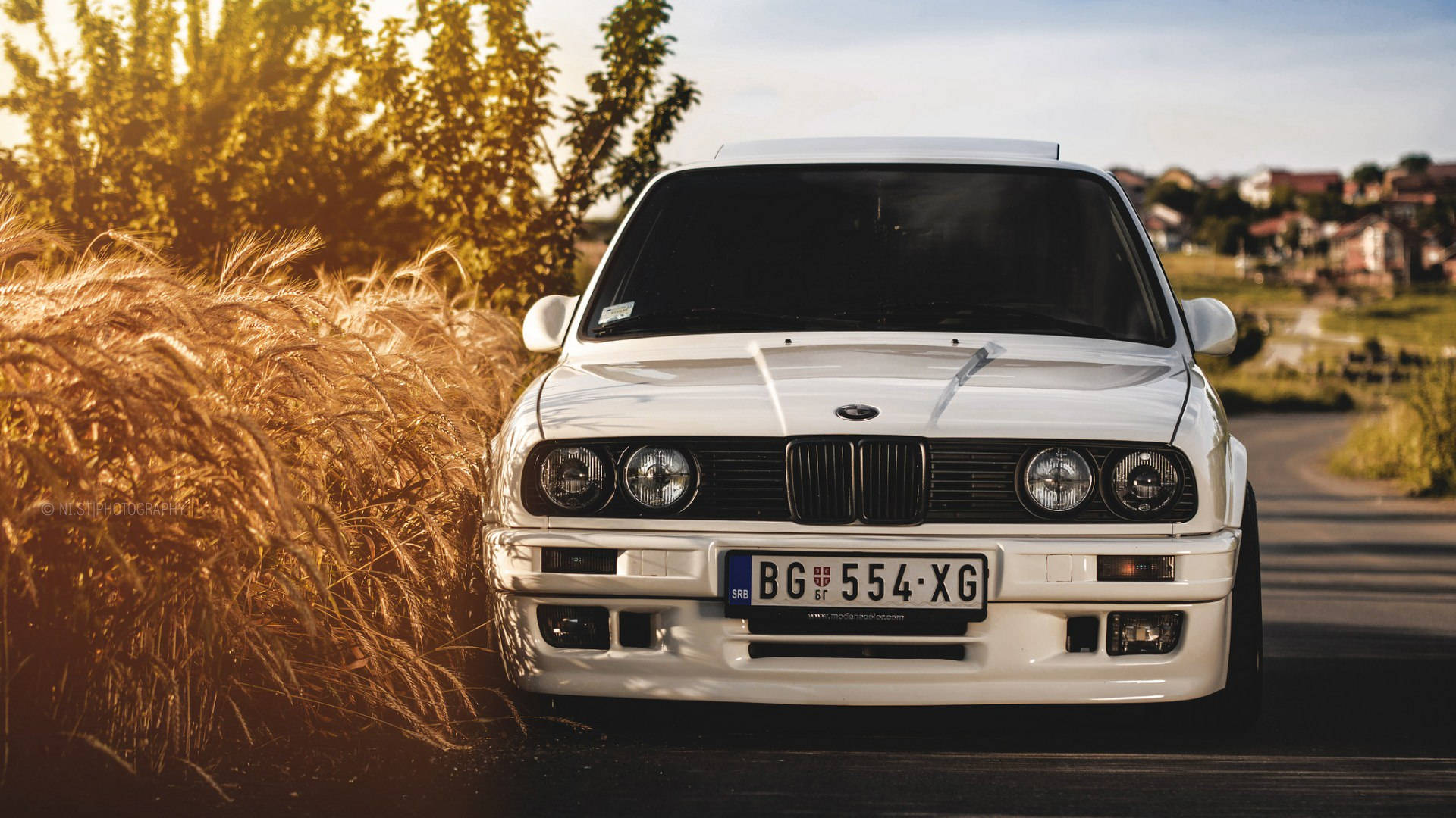 汽車 桌布 壁紙 — 一輛純白色的BMW E30跑車停在日落時分金色麥田旁的鄉村道路上。
