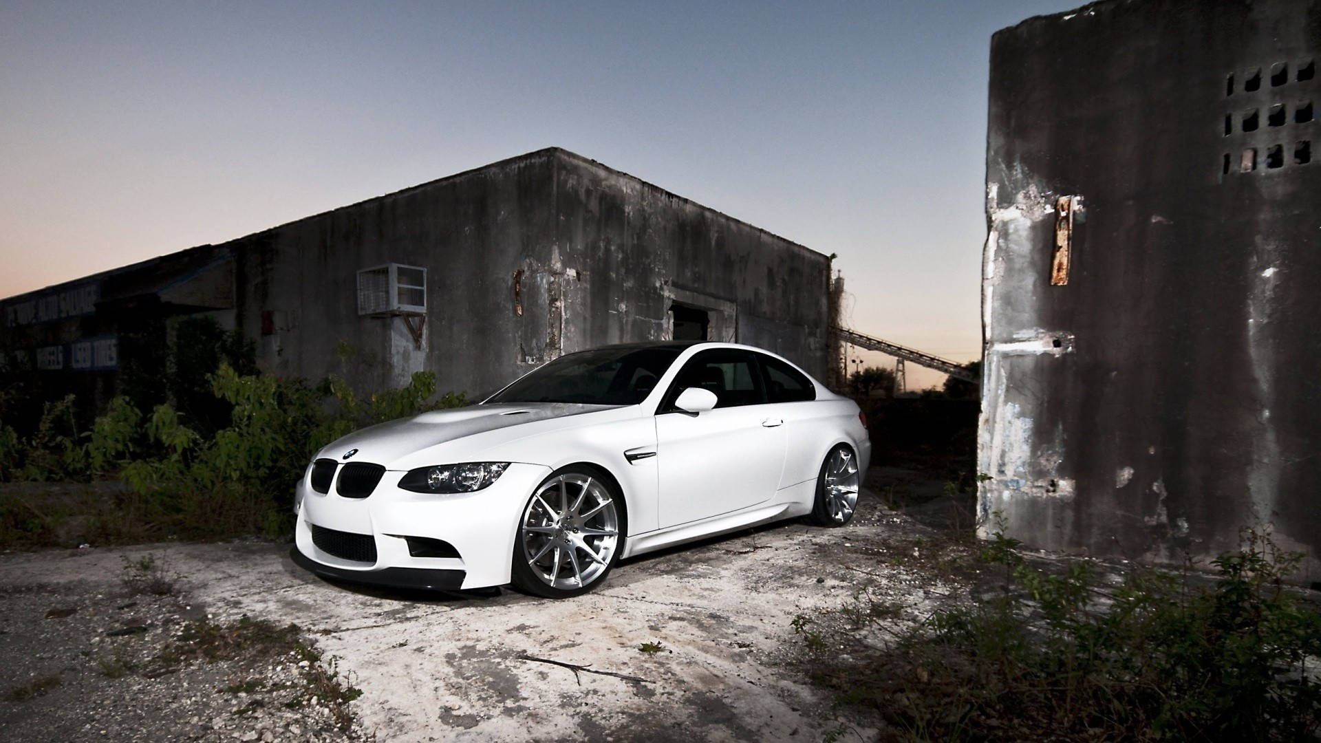 m 桌布 壁紙 — 一輛純白色的BMW M3雙門轎跑車在黃昏時停泊在破舊的工業建築之間。