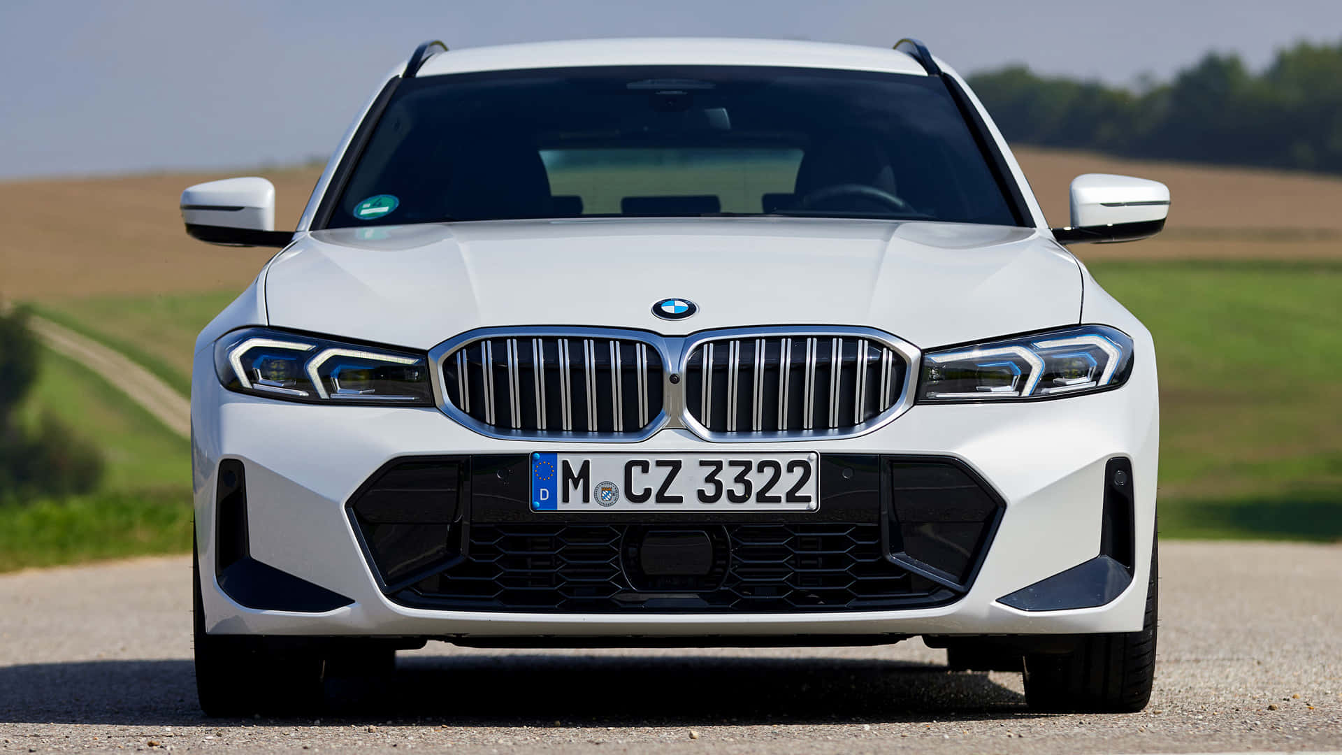 Bmw 328 桌布 壁紙 — 一輛純白色的BMW SUV在晴朗天空下，面向碎石路上的起伏綠色和棕色田野。