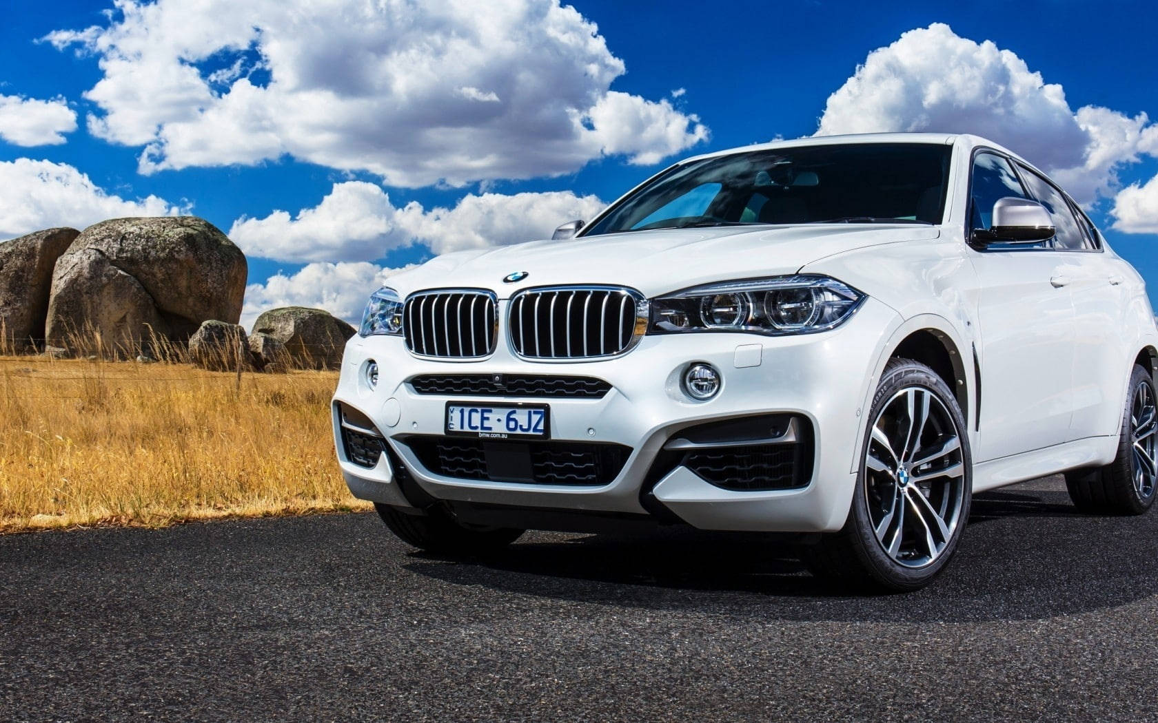 m 桌布 壁紙 — 一輛純白色的BMW X5 SUV停泊在瀝青路上，背景是湛藍的天空、蓬鬆的白雲和巨大的岩石。