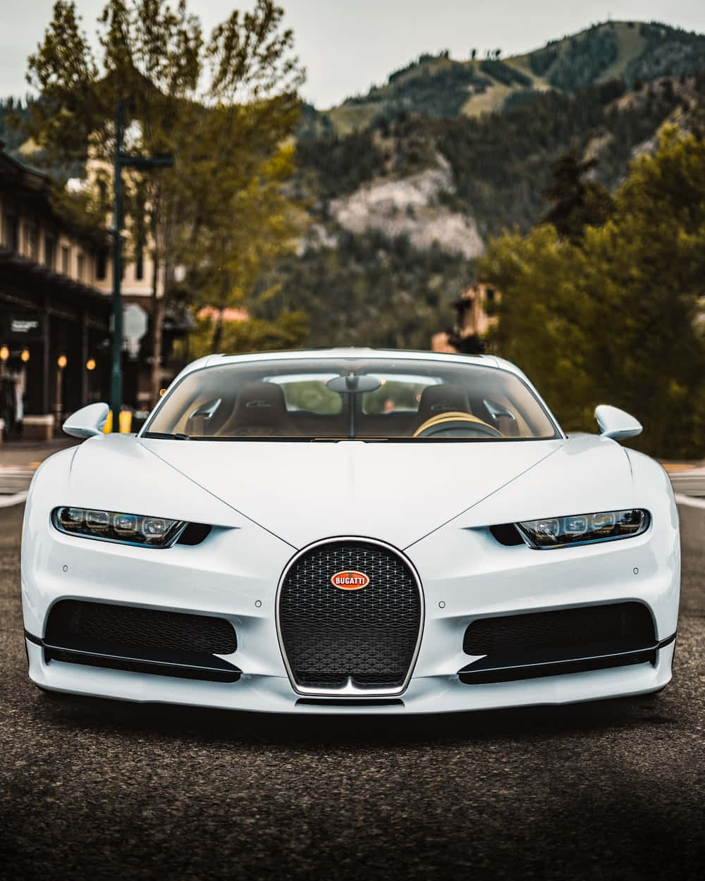 Best Bugatti 桌布 壁紙 — 一輛純白色的Bugatti Chiron在山城街道上向前行駛，背景是茂密的綠樹和岩石山丘。
