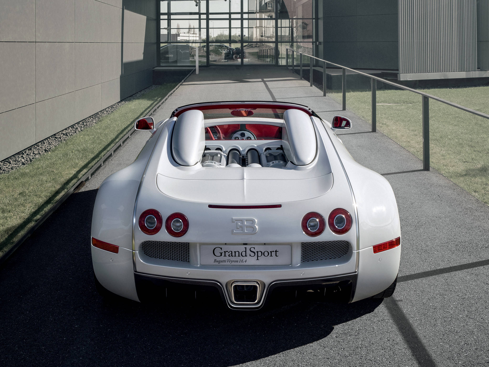 bugatti iPhone 桌布 壁紙 — 一輛純白色的Bugatti Veyron Grand Sport敞篷車停放在現代鋪砌的人行道上，背景是玻璃建築。