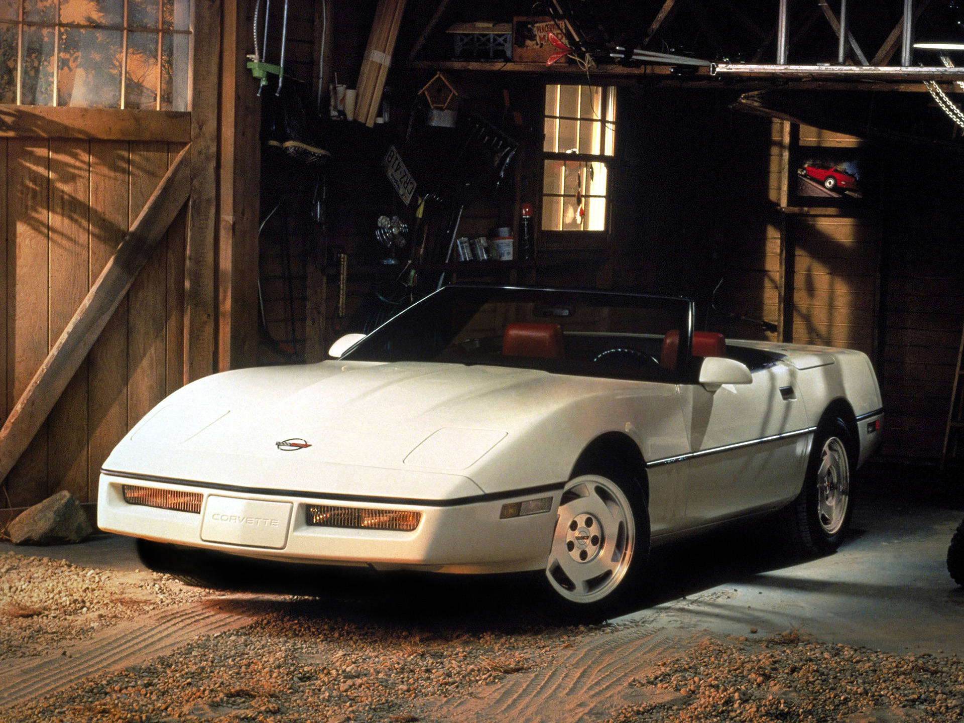 corvette 桌布 壁紙 — 一輛純白色的Corvette敞篷車停放在一個充滿溫暖陽光的質樸木車庫內。