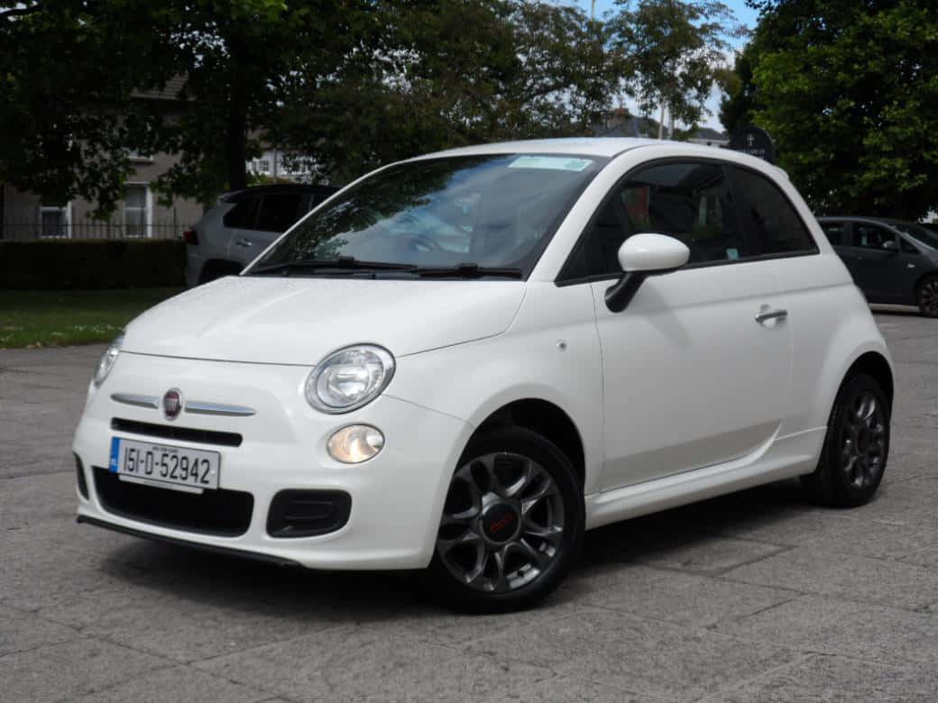 Fiat 桌布 壁紙 — 一輛純白色的Fiat 500停放在鋪砌的停車場上，背景有綠樹和房屋，在日光下。