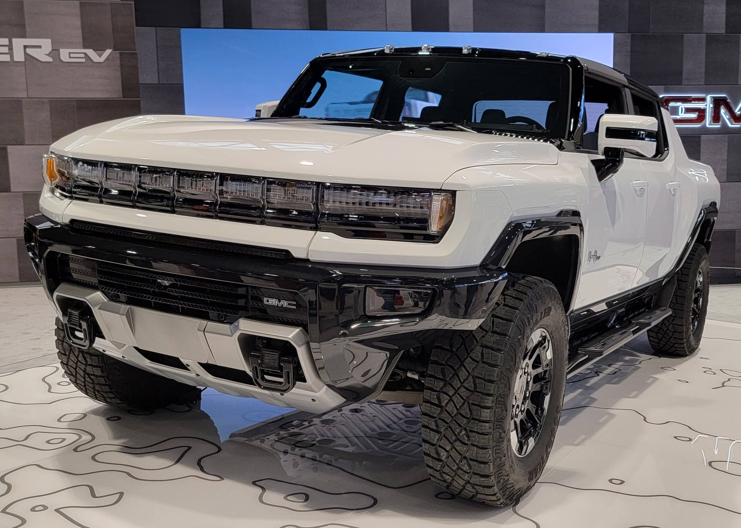 Truck 桌布 壁紙 — 一輛純白色的GMC Hummer EV電動皮卡車在車展上展出，帶有醒目的黑色飾邊和堅固的輪胎。