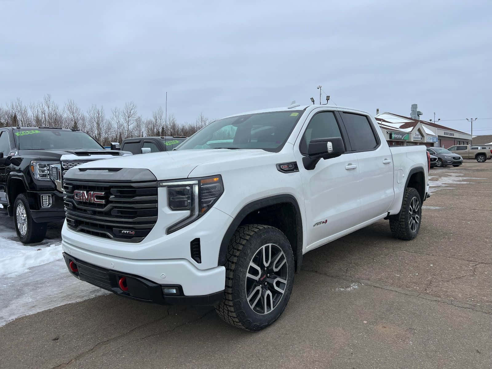 Gmc Sierra 桌布 壁紙 — 一輛純白色的GMC Sierra AT4 pickup卡車停放在雪地停車場，周圍有光禿禿的樹木和陰天。