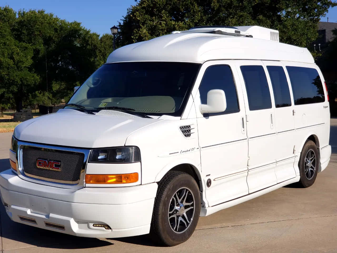 Gmc Savana 桌布 壁紙 — 一輛純白色的GMC露營車停在陽光明媚的日子裡，背景是茂密的綠樹。