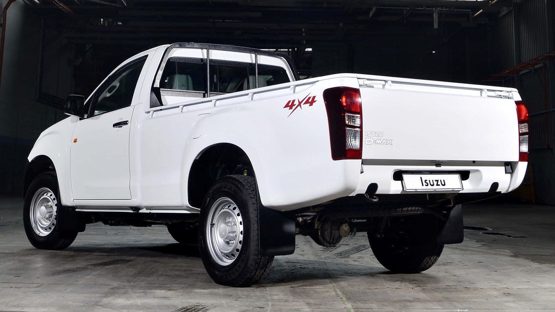 Isuzu 桌布 壁紙 — 一輛純白色的五十鈴 D-MAX 4x4 皮卡車在光線昏暗的工業車庫內從後方四分之三角度展示。
