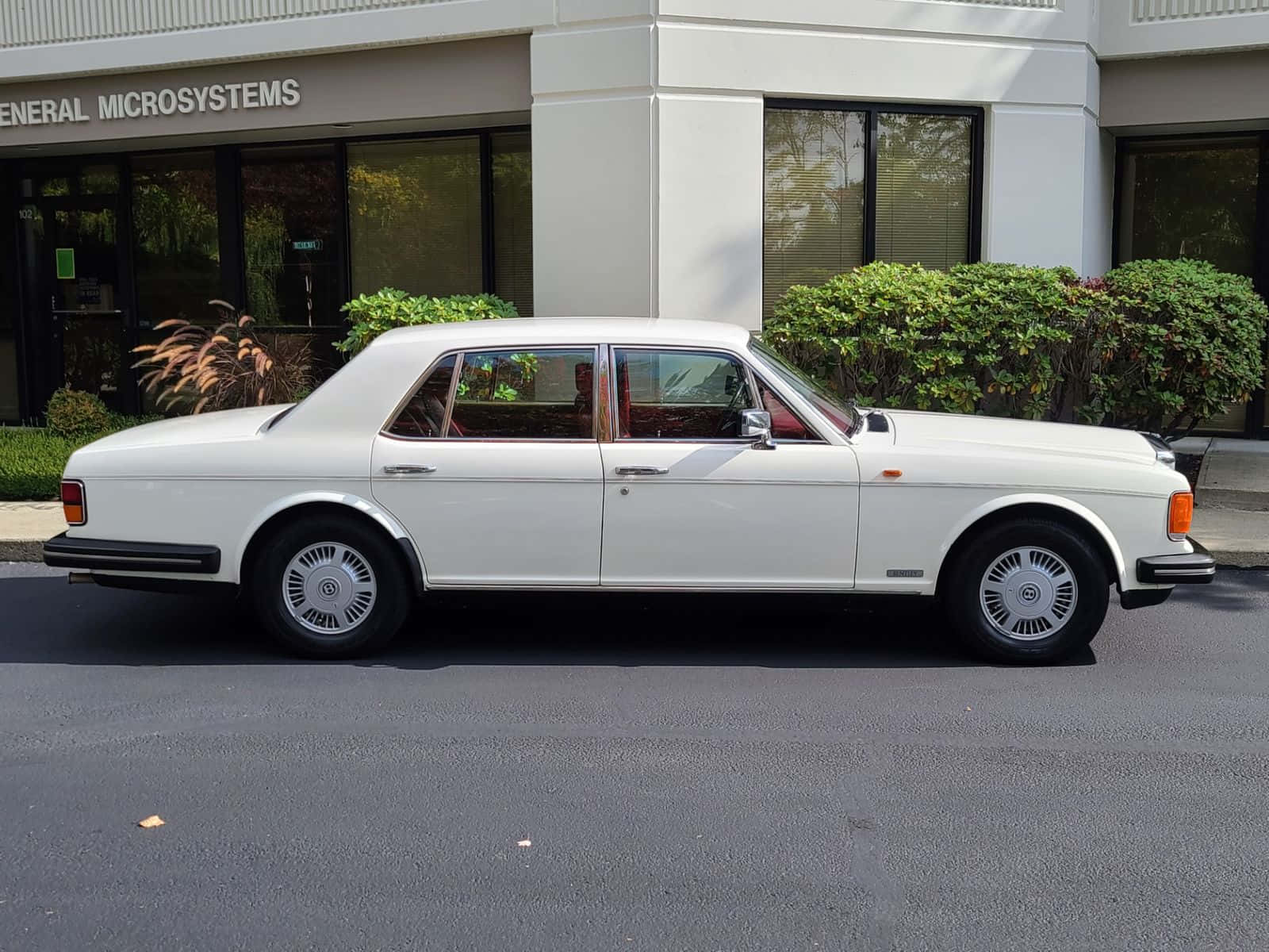 Bentley Eight 桌布 壁紙 — 一輛純白色的勞斯萊斯銀影 II 停放在現代辦公大樓前的柏油路上，周圍有綠色灌木。