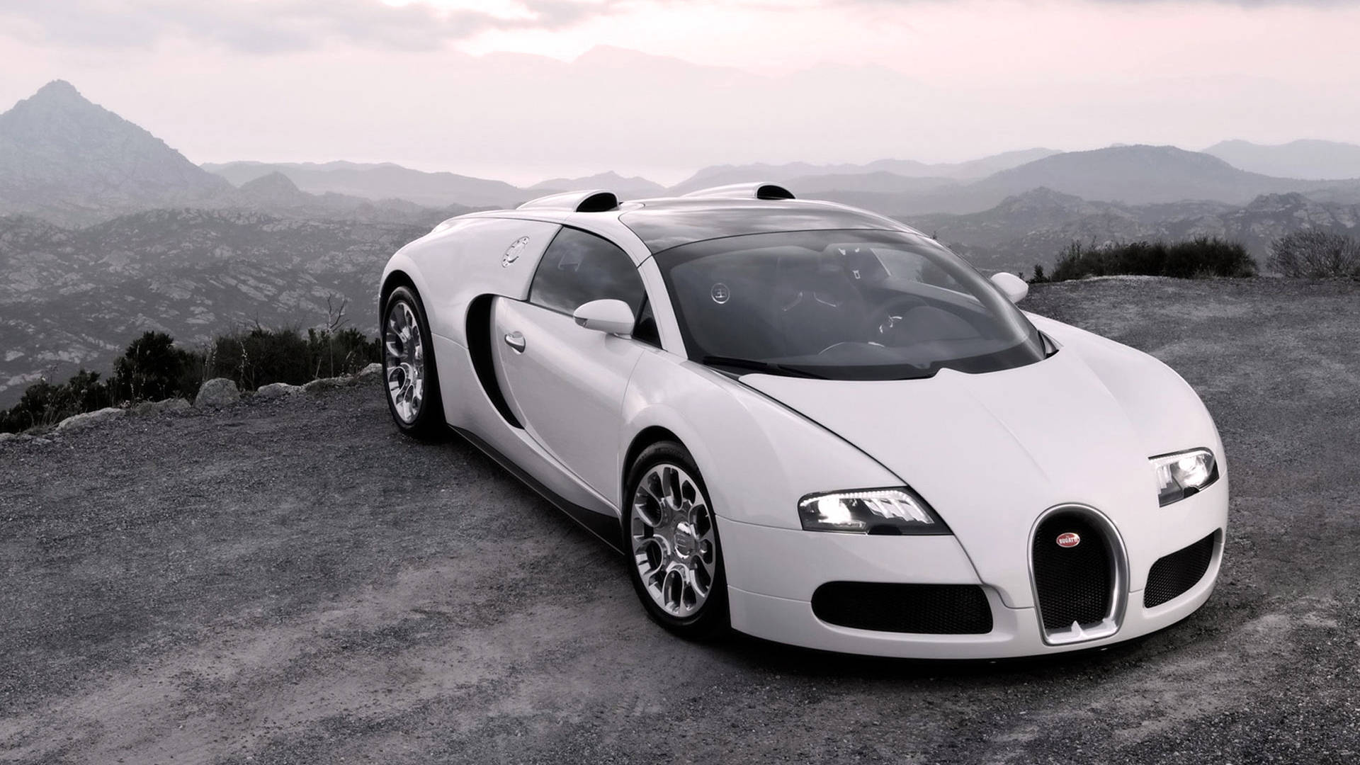 Cool Bugatti 桌布 壁紙 — 一輛純白色的布加迪超級跑車停泊在崎嶇的懸崖上，俯瞰著薄霧籠罩的山脈，背景是柔和的黃昏天空。
