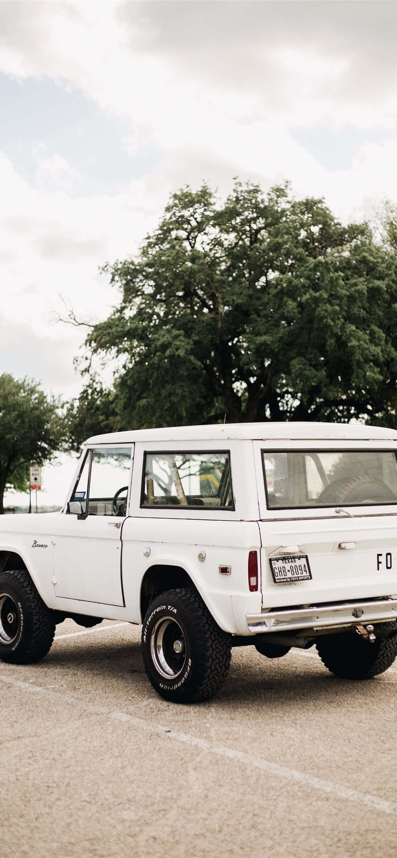 電玩遊戲 桌布 壁紙 — 一輛純白色的復古Jeep Wrangler停在瀝青路面上，天空多雲，背景是茂密的綠樹。