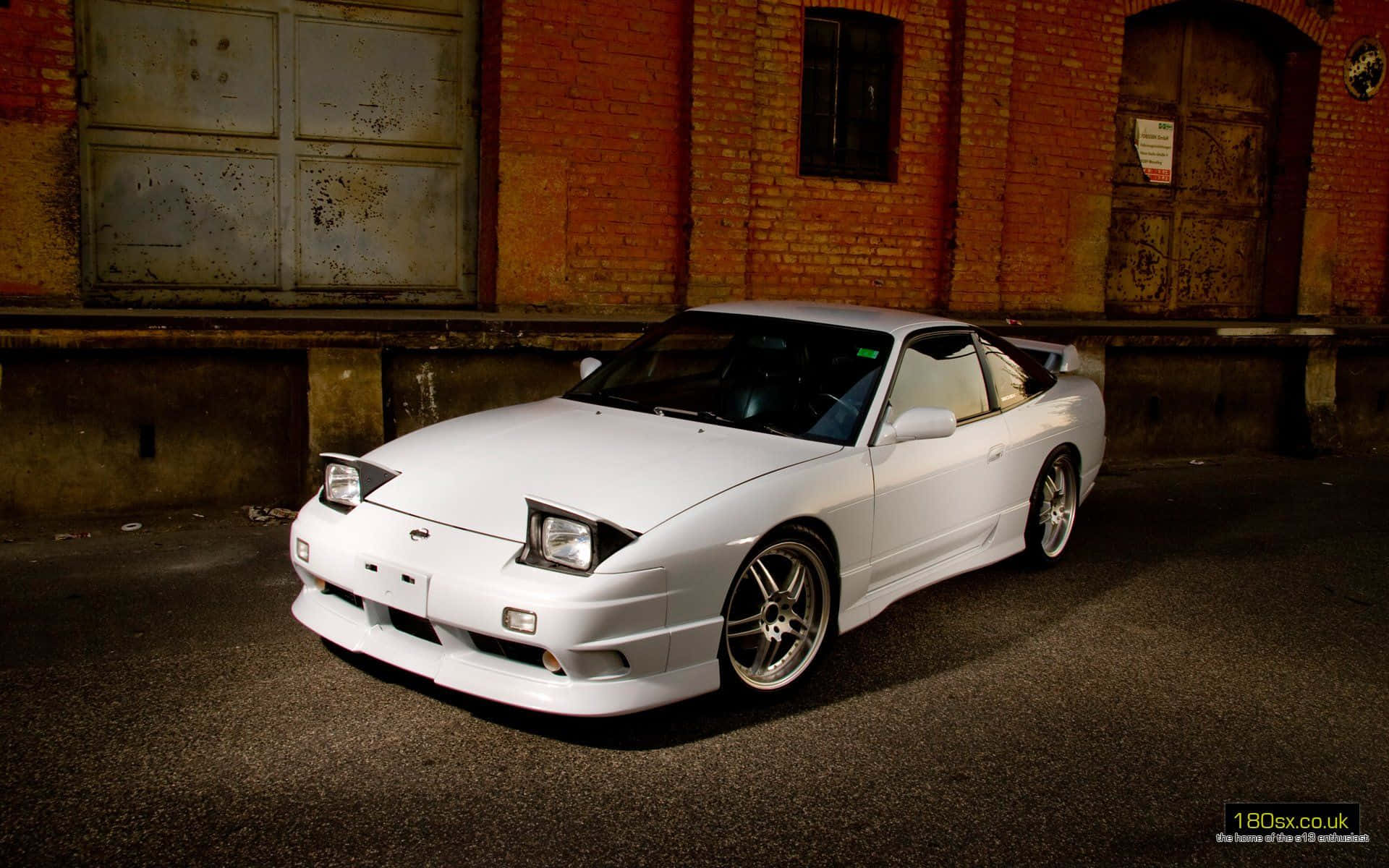 Nissan Silvia S13 桌布 壁紙 — 一輛純白色的日產300ZX跑車停泊在風化的磚砌建築前，在戲劇性的燈光下。