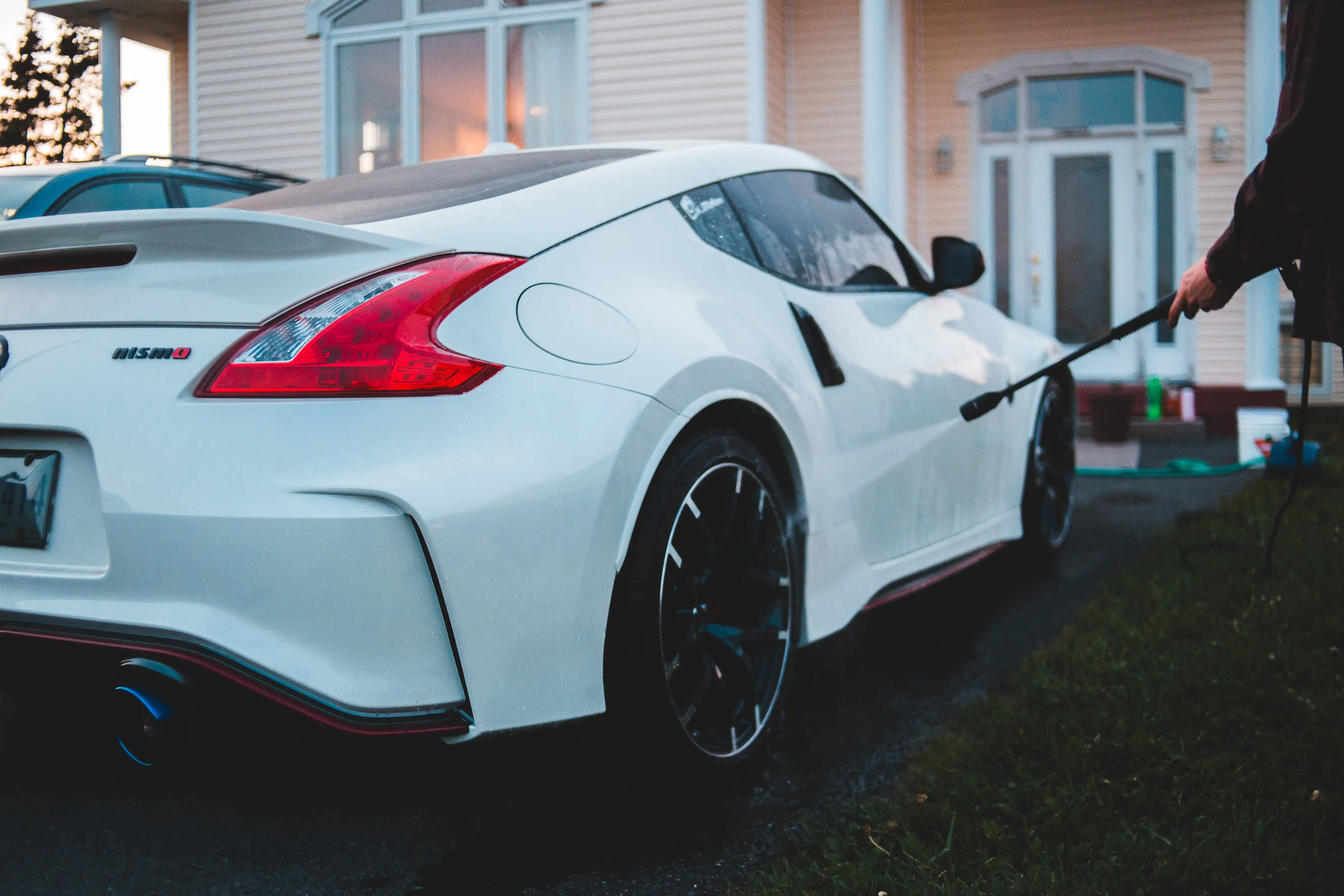 Nissan 桌布 壁紙 — 一輛純白色的日產370Z Nismo在黃昏時分於郊區房屋前用水管清洗。