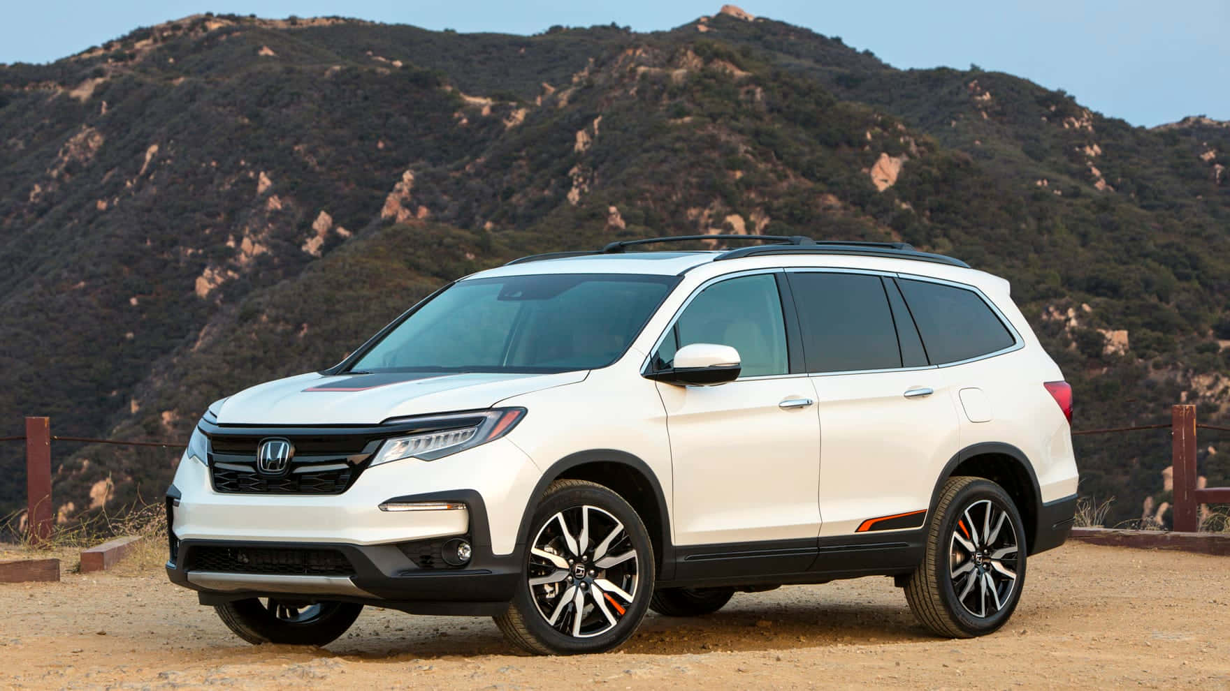Honda Pilot 桌布 壁紙 — 一輛純白色的本田Pilot SUV停放在塵土飛揚的地形上，背景是崎嶇的山脈和清澈的藍天。